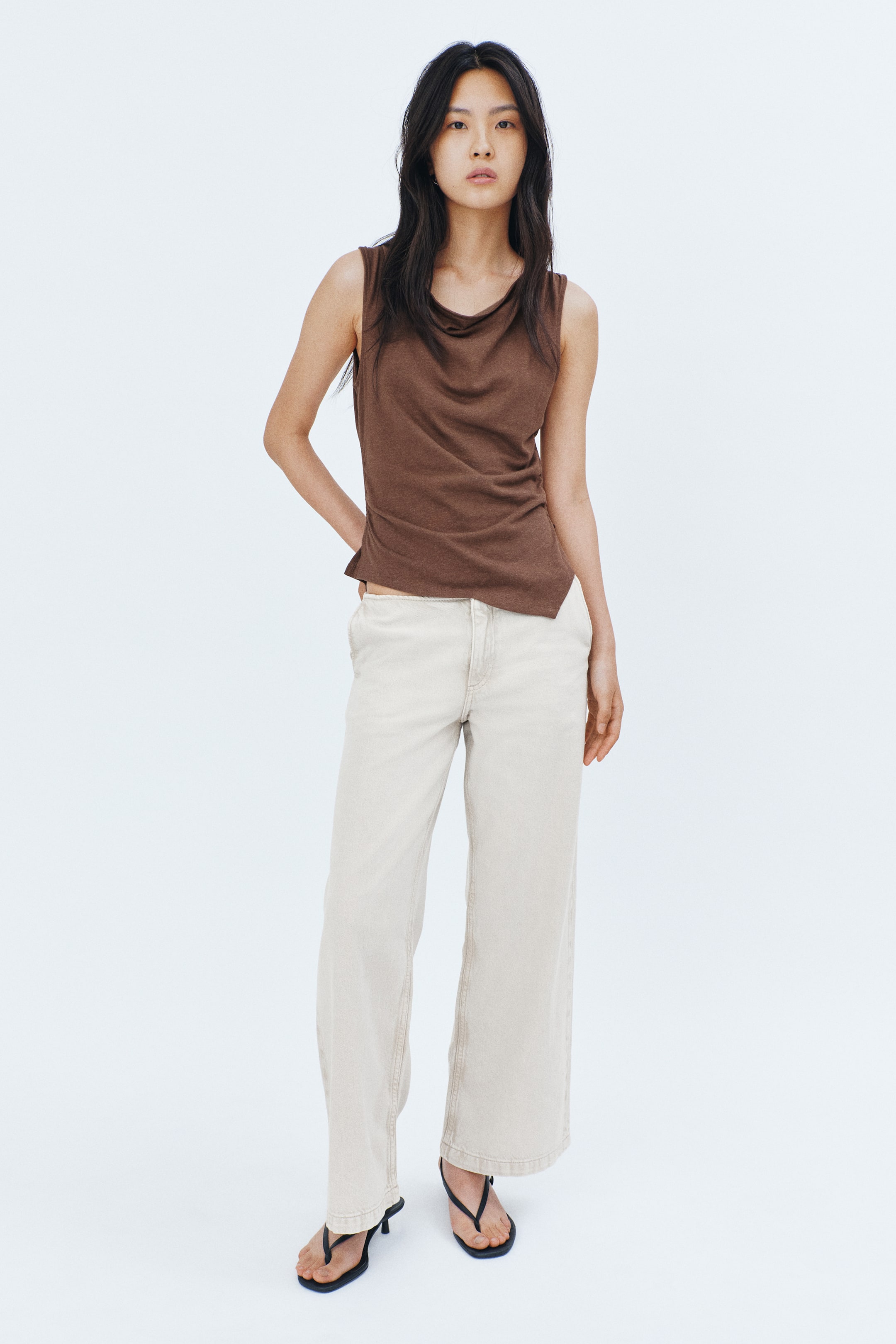 View larger image: Model tersebut mengenakan baju tanpa lengan berwarna coklat, dengan leher cowl, berkumpul di sisi untuk mencipta efek drape, dan mempunyai hem asimetrik, dipadankan dengan seluar berwarna cerah.