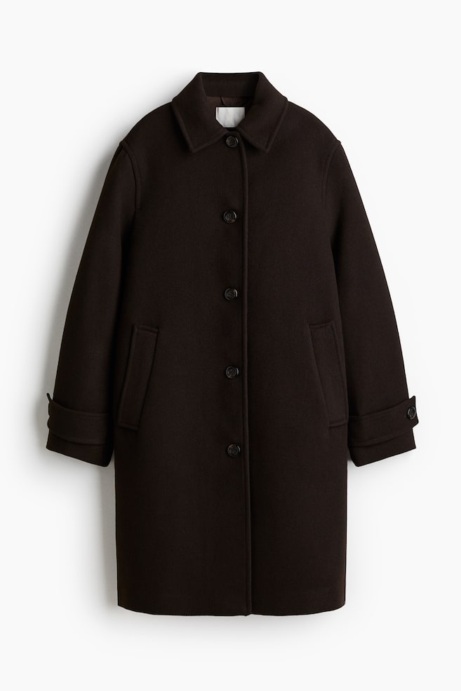 A dark brown coat is being displayed from the front, featuring a pointed collar and a four-button front closure. It is designed with two front welt pockets and long sleeves with cuffs folded back and secured by button tabs. - 1