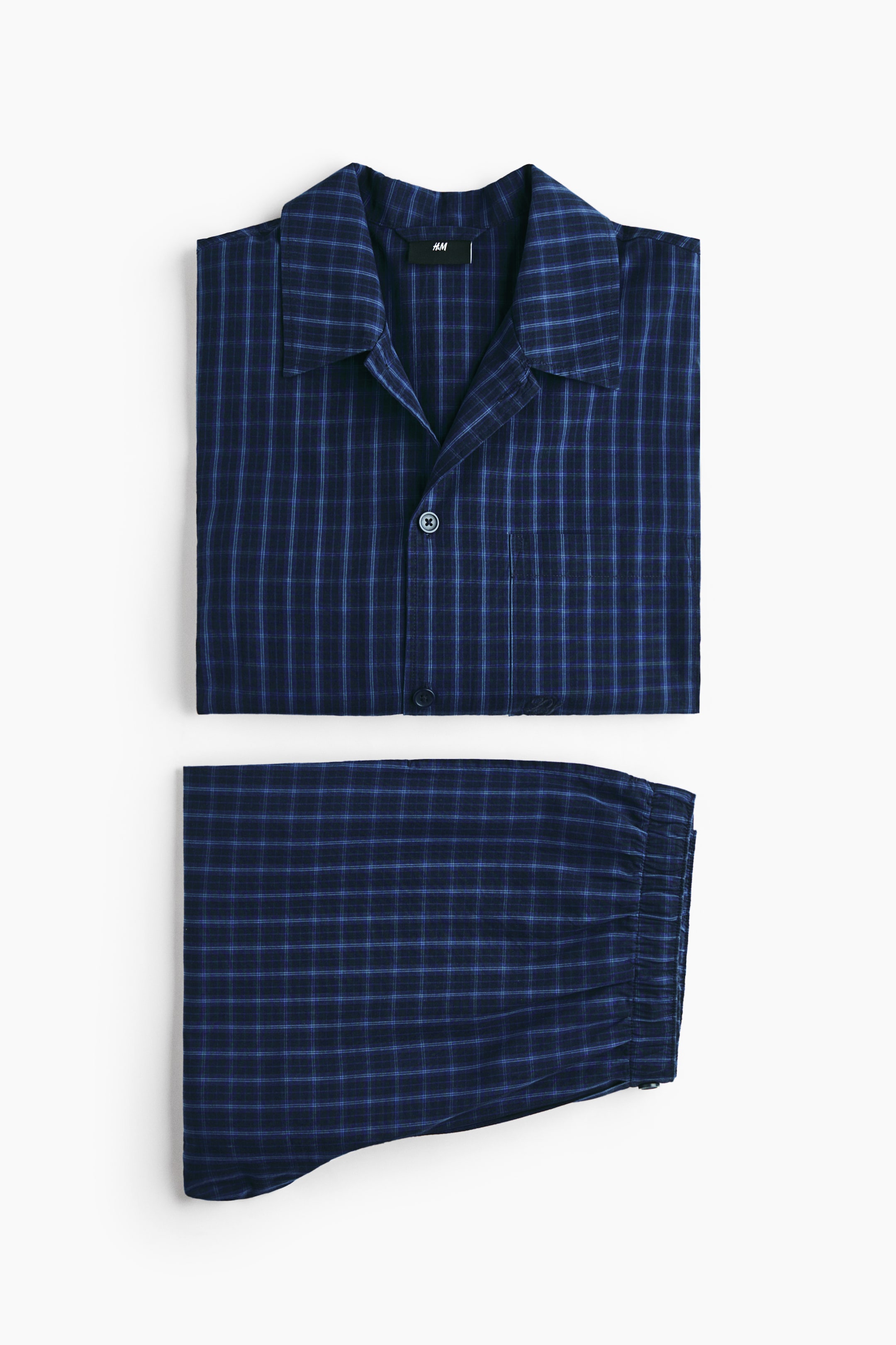 View larger image: Presenting a set of pyjamas, featuring a folded shirt and folded bottoms. The dark blue shirt showcases a light blue plaid pattern, a turn-down collar, a French front with visible buttons, and a chest pocket with a subtle embroidered detail. The matching bottoms display an elasticated waist on the side.