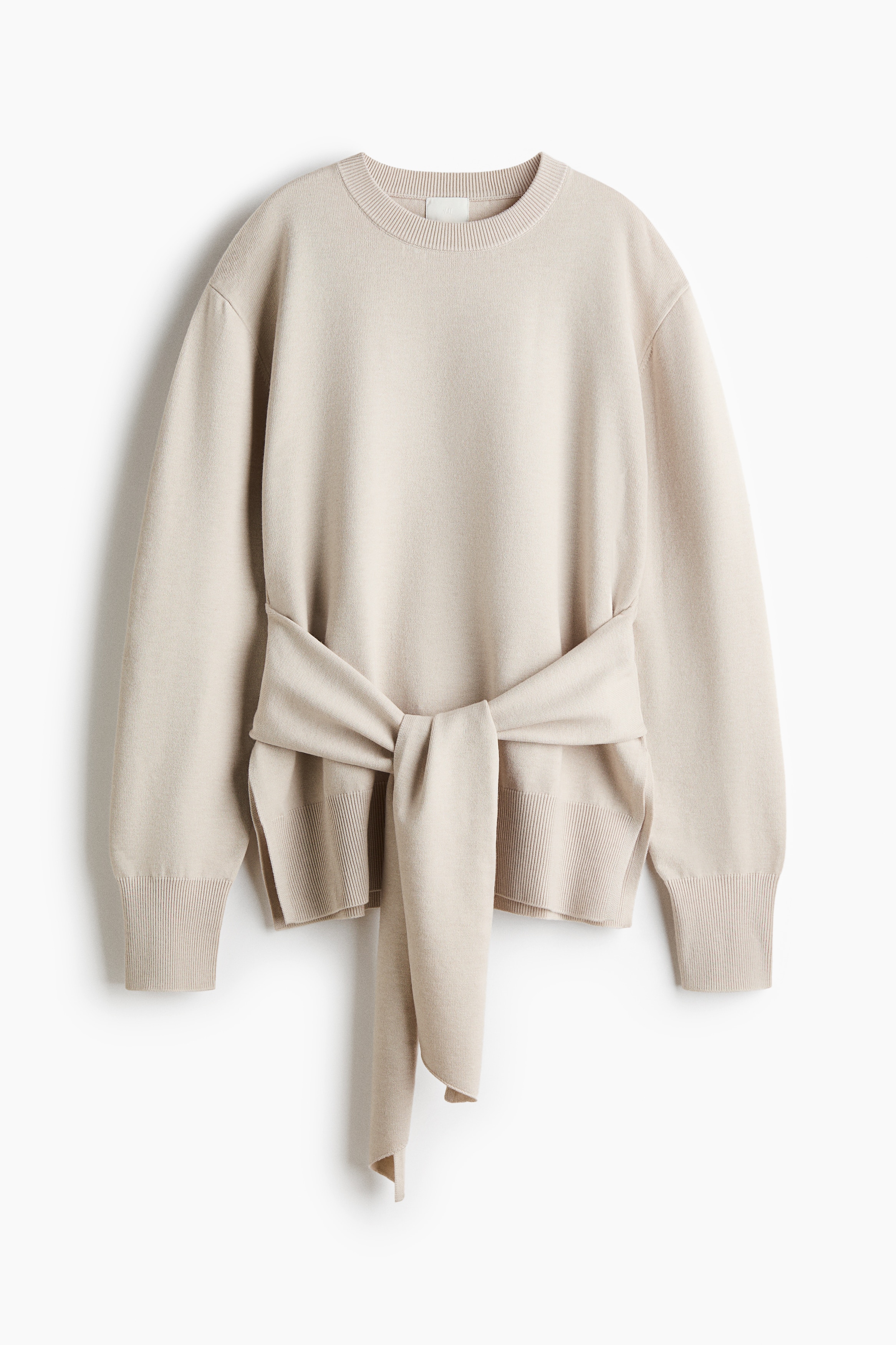 A light beige, fine-knit sweater is shown from the front, featuring a round ribbed neckline, dropped shoulders and long sleeves with ribbed cuffs. The sweater features wide, self-fabric ties knotted at the front waist and is finished with a ribbed hem.