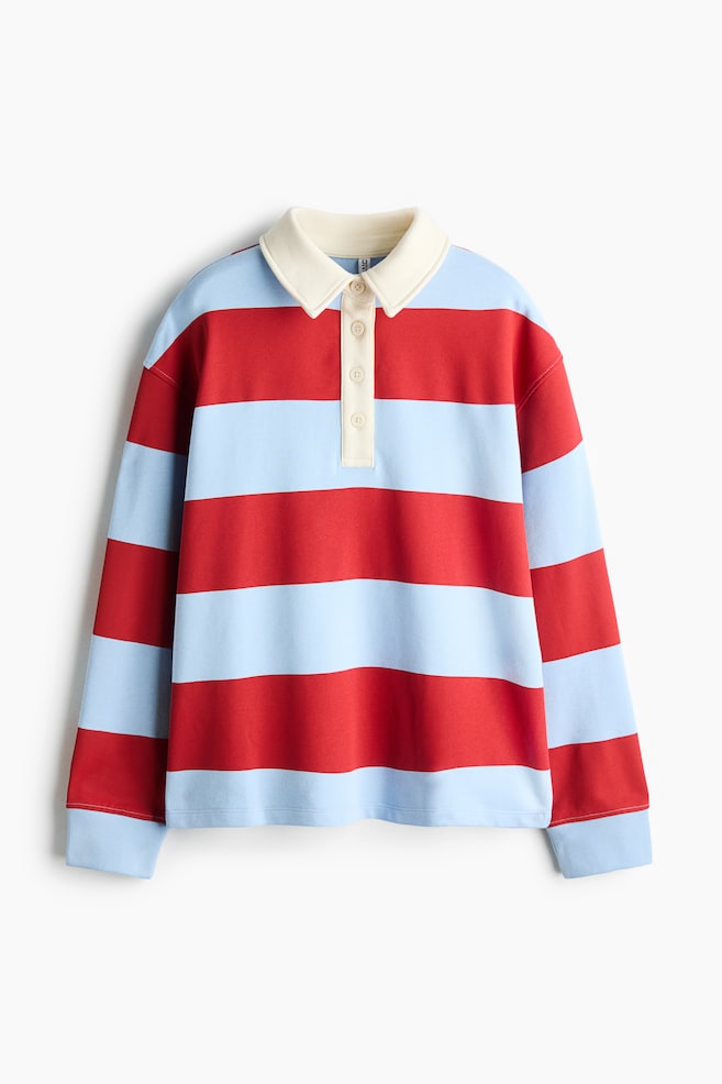 A long-sleeved rugby shirt is facing front, displaying wide horizontal stripes in alternating red and light blue. The shirt is featuring a contrasting cream-colored polo collar with a matching four-button partial placket and light blue ribbed cuffs. - 1