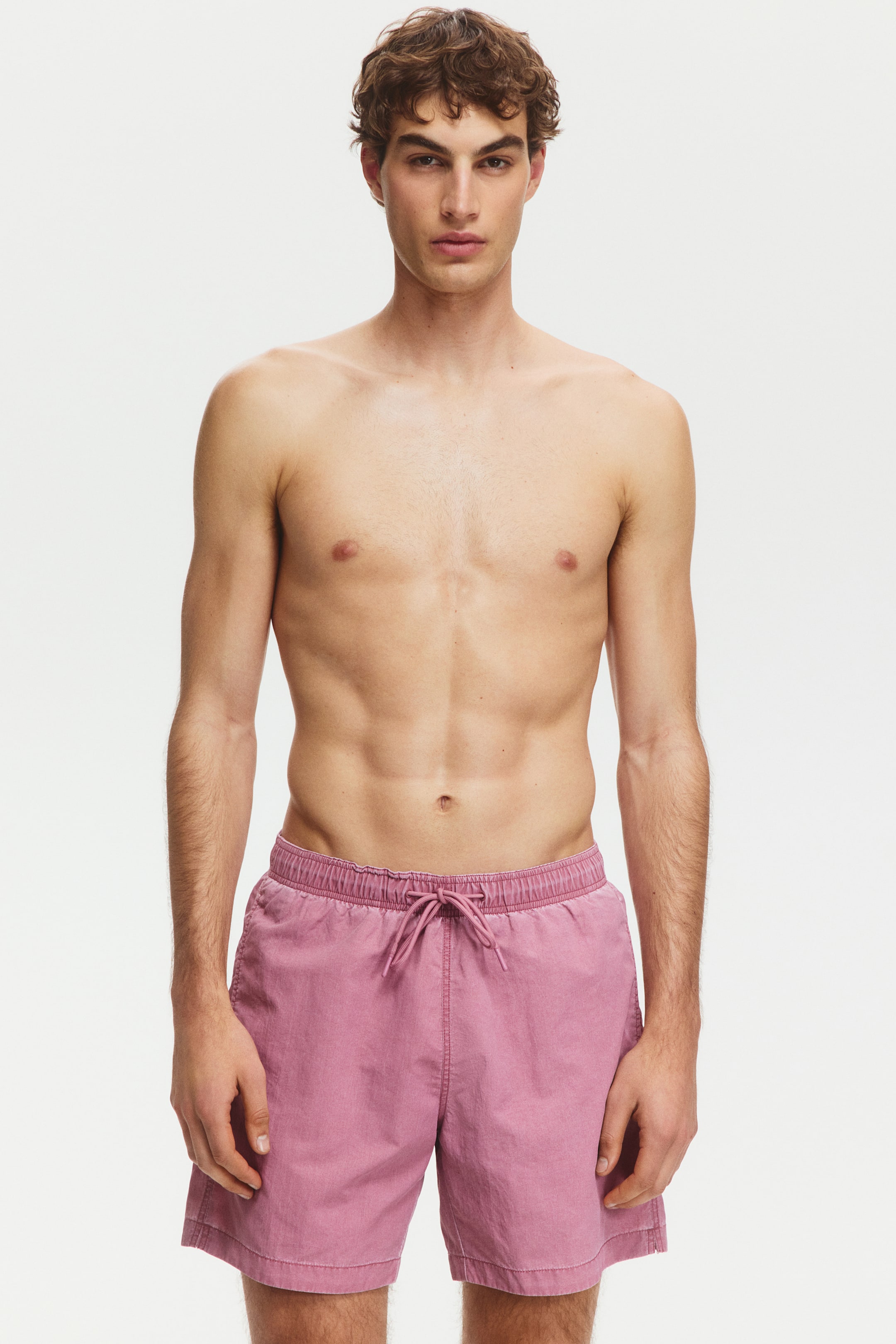 Visa större bild: Dämpade rosa shorts, tillverkade av ett tvättat tyg, bärs framåt. De har en elastisk midja med en matchande rosa dragsko knuten i mitten, och fållen vilar på mitten av låret.