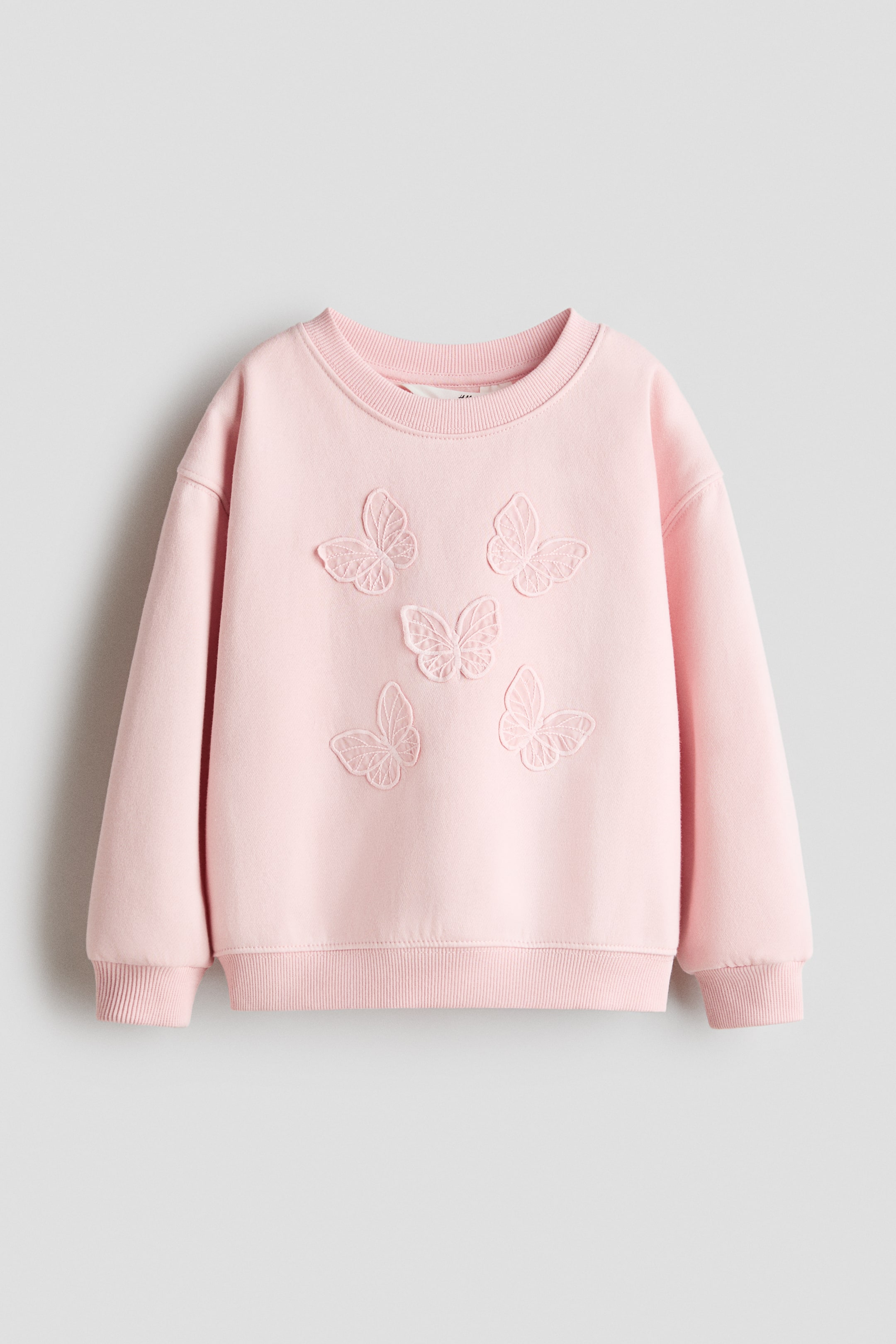 הצגת תמונה גדולה יותר: סווטשירט ורוד, FRONT, כולל צווארון עגול מצולע, חפתים מצולעים ושוליים מצולעים. חמישה קישוטי פרפרים רקומים מקשטים את החלק הקדמי של הסווטשירט.
