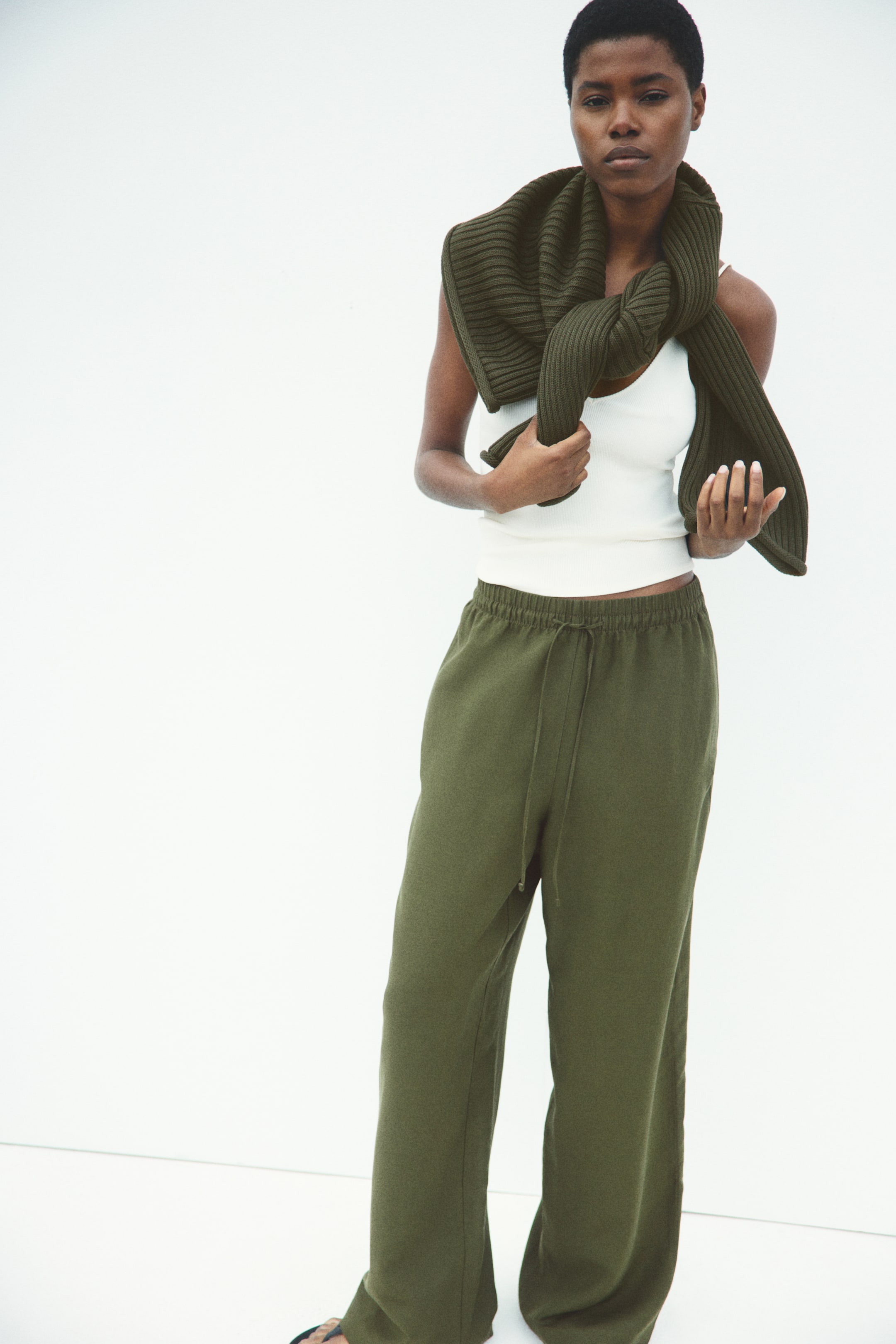 View larger image: Olive green, loose-fit trousers in an airy weave crafted from a linen blend are showcased by the model. They boast a high, elasticized waist with a slender drawstring, subtle side pockets, and straight legs.