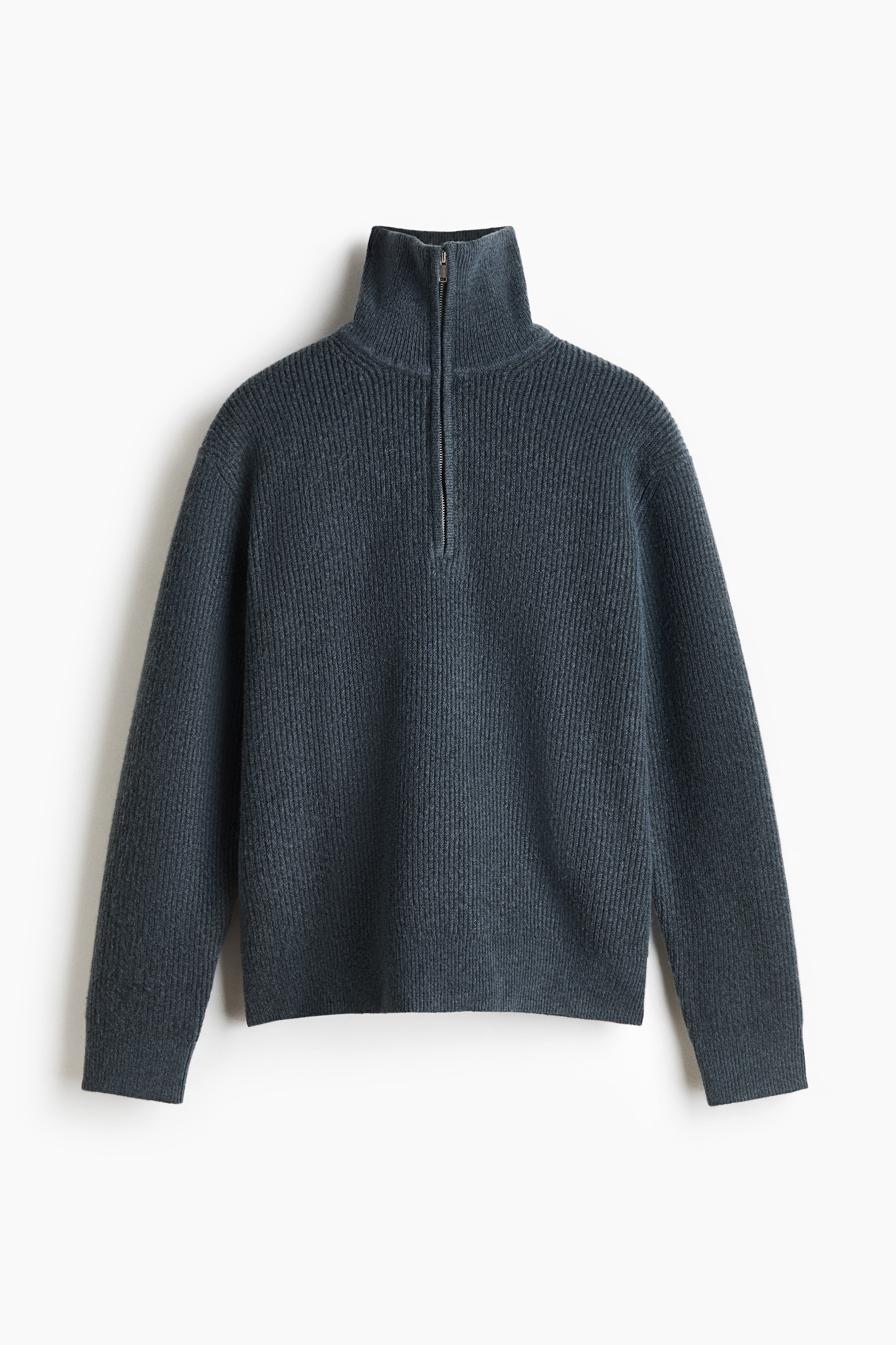 A dark grey, rib-knit sweater with a half-zip collar is being worn by the model, who is standing with arms crossed. The relaxed-fit sweater is layered over a white crew-neck T-shirt and styled with black jeans.