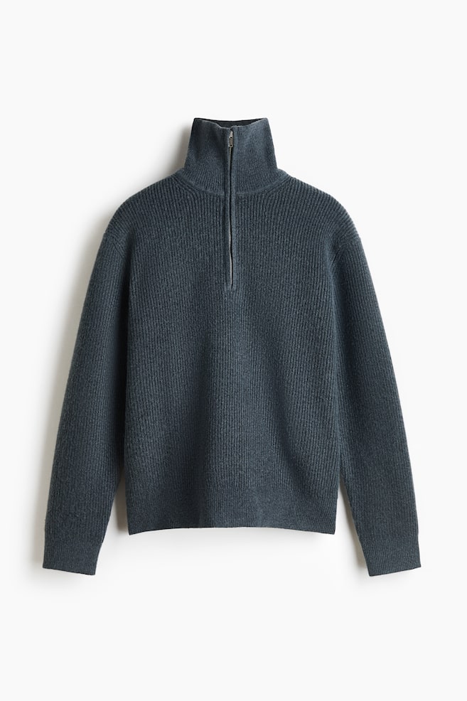 Un pull demi-zip en maille côtelée gris foncé est présenté de face, avec un col montant à entonnoir et une fermeture éclair argentée. Le pull met en valeur une texture côtelée verticale sur lâensemble du modèle, avec des manches longues, des poignets côtelés et un ourlet droit. - 1