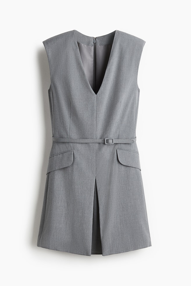 A grey sleeveless dress is shown from the front, featuring a deep V-neckline and structured shoulders. It is cinching at the waist with a thin, matching belt and buckle, and is presenting two curved flap pockets, while a central pleat is detailing the front skirt. - 1