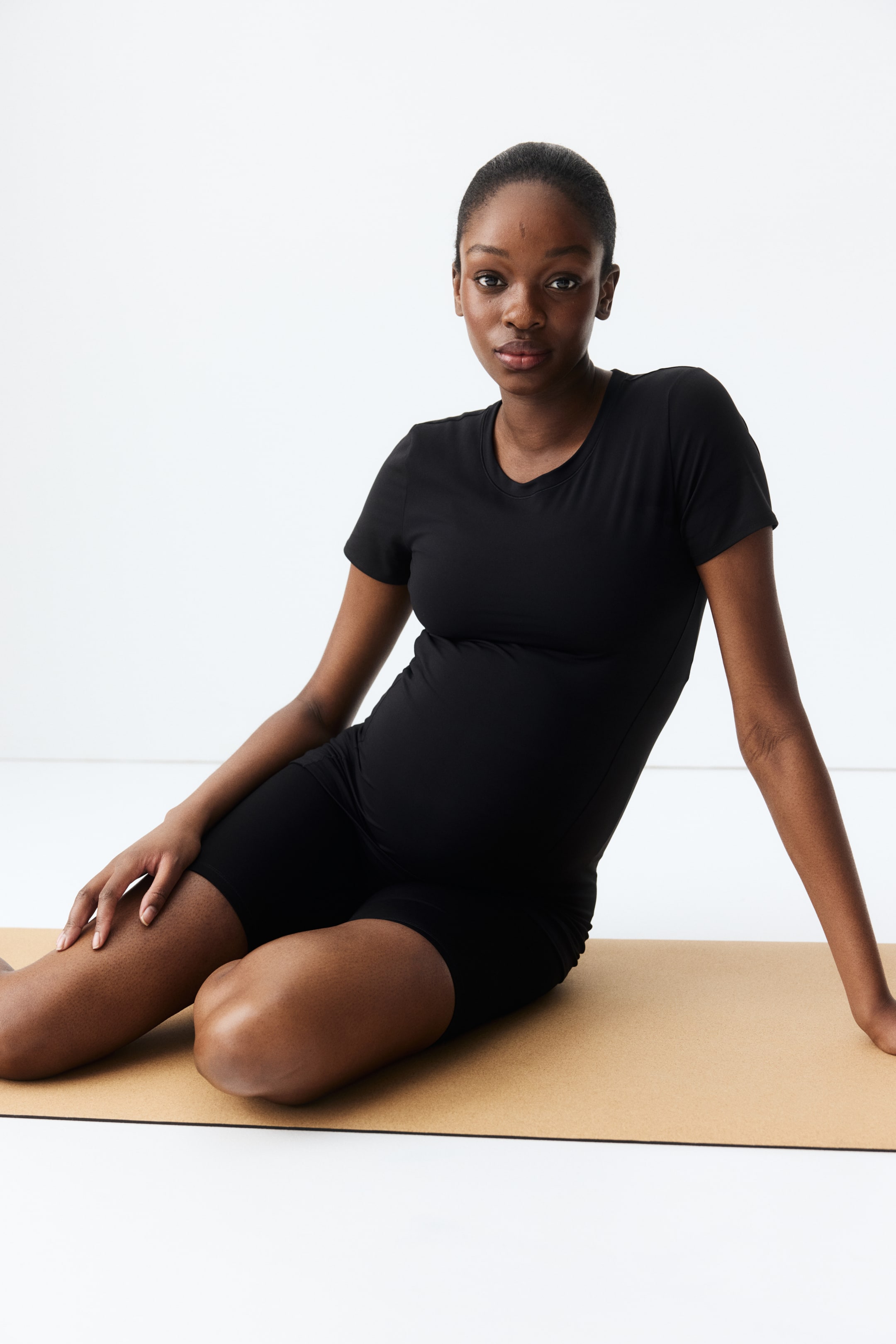 Ampliar la imagen: Un top negro de manga corta presenta un cuello redondo y se ajusta ceñidamente alrededor de una barriga embarazada. Unos shorts negros a juego se extienden hasta la mitad del muslo, parecen de cintura alta y ajustados.