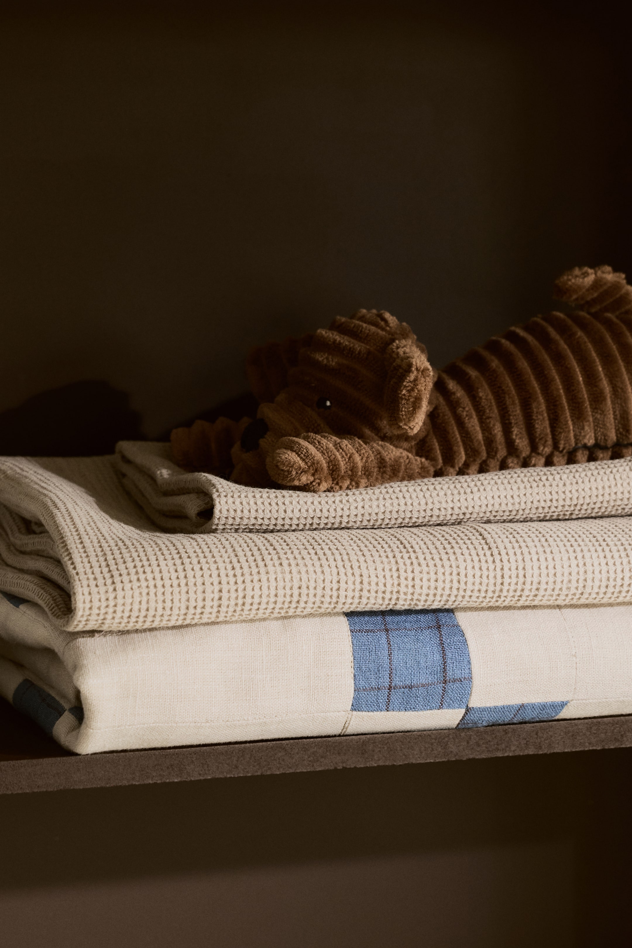 Nagyobb kép megtekintése: "Gofrizott baba takaró, világos krémszínben, összehajtva és laposan elhelyezve, megmutatva jellegzetes gofri kötésű textúráját. Jelenleg a textíliák rendezett halmának középső elemeként van elhelyezve."