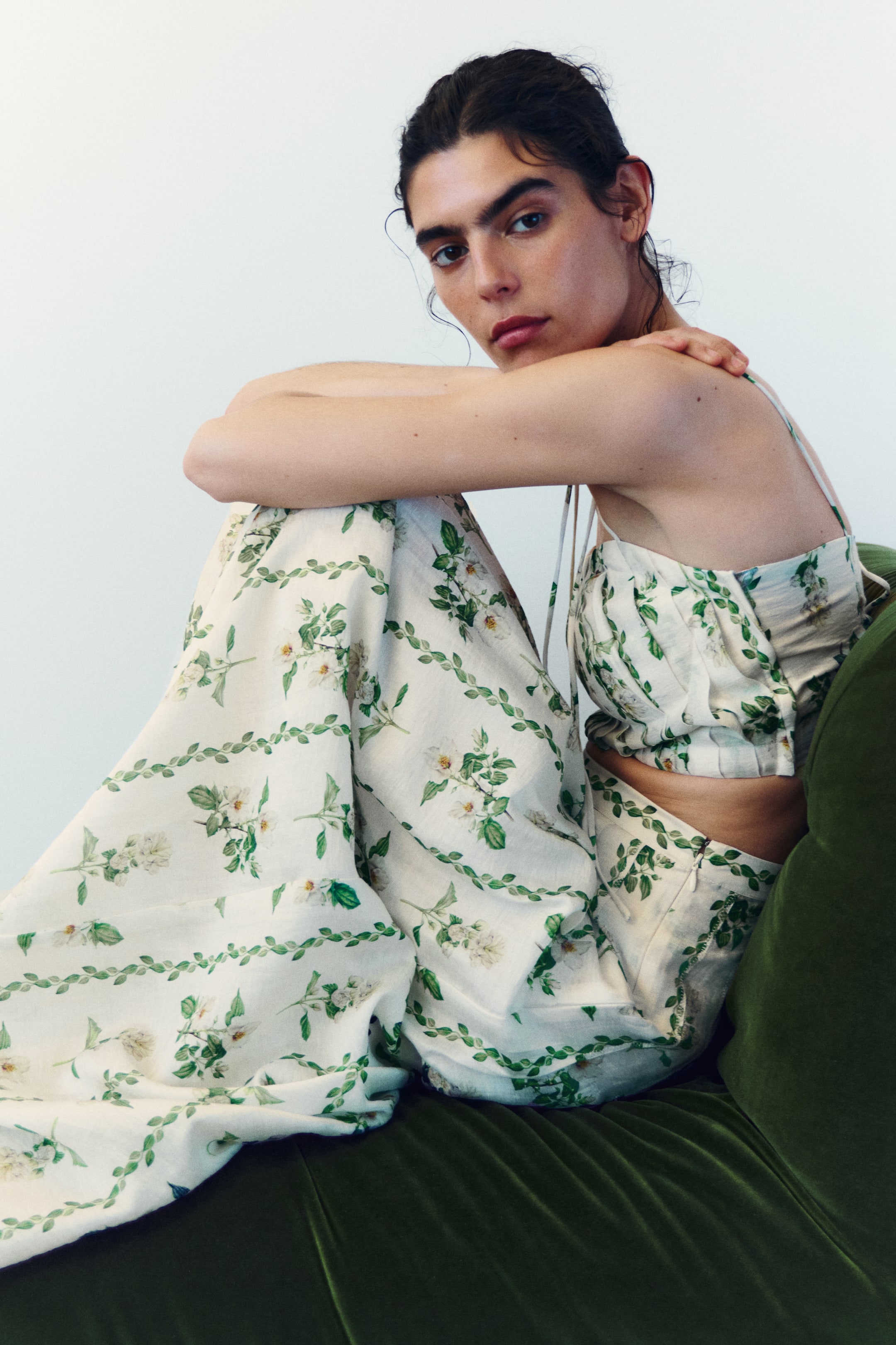 Ver imagen más grande: Un conjunto de dos piezas compuesto por un top corto y pantalones de pierna ancha, ambos estampados con flores blancas y enredaderas verdes sobre una tela ligera. El top corto presenta finos tirantes tipo espagueti y un busto fruncido, mientras que los pantalones muestran un corte relajado y de pierna ancha.