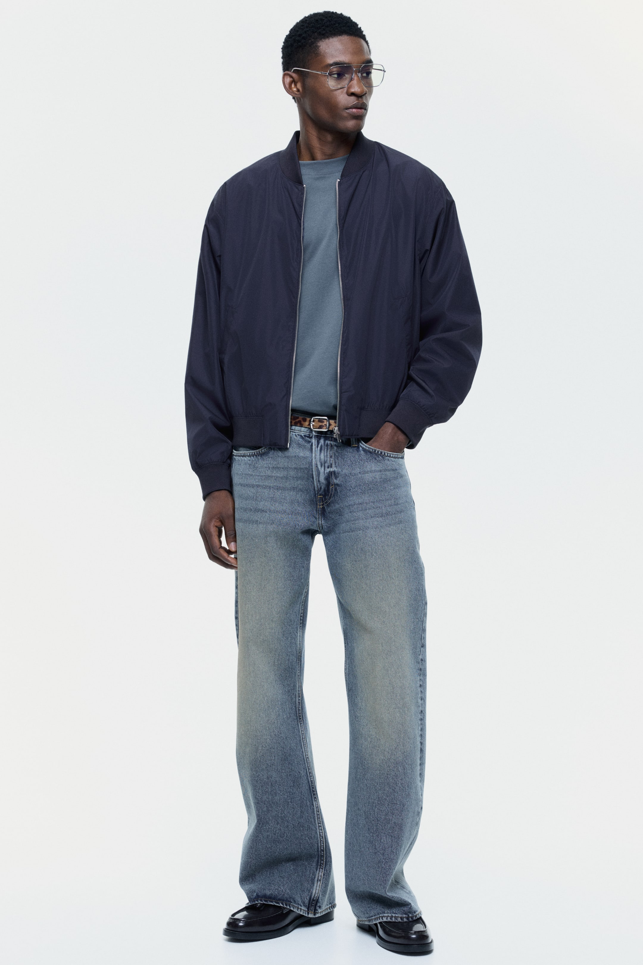 View larger image: This dark navy bomber jacket is highlighted by its ribbed stand-up collar, a full-zip front with a silver zipper, and long sleeves with ribbed cuffs. It features a relaxed fit and a ribbed hem, styled open over a blue t-shirt.