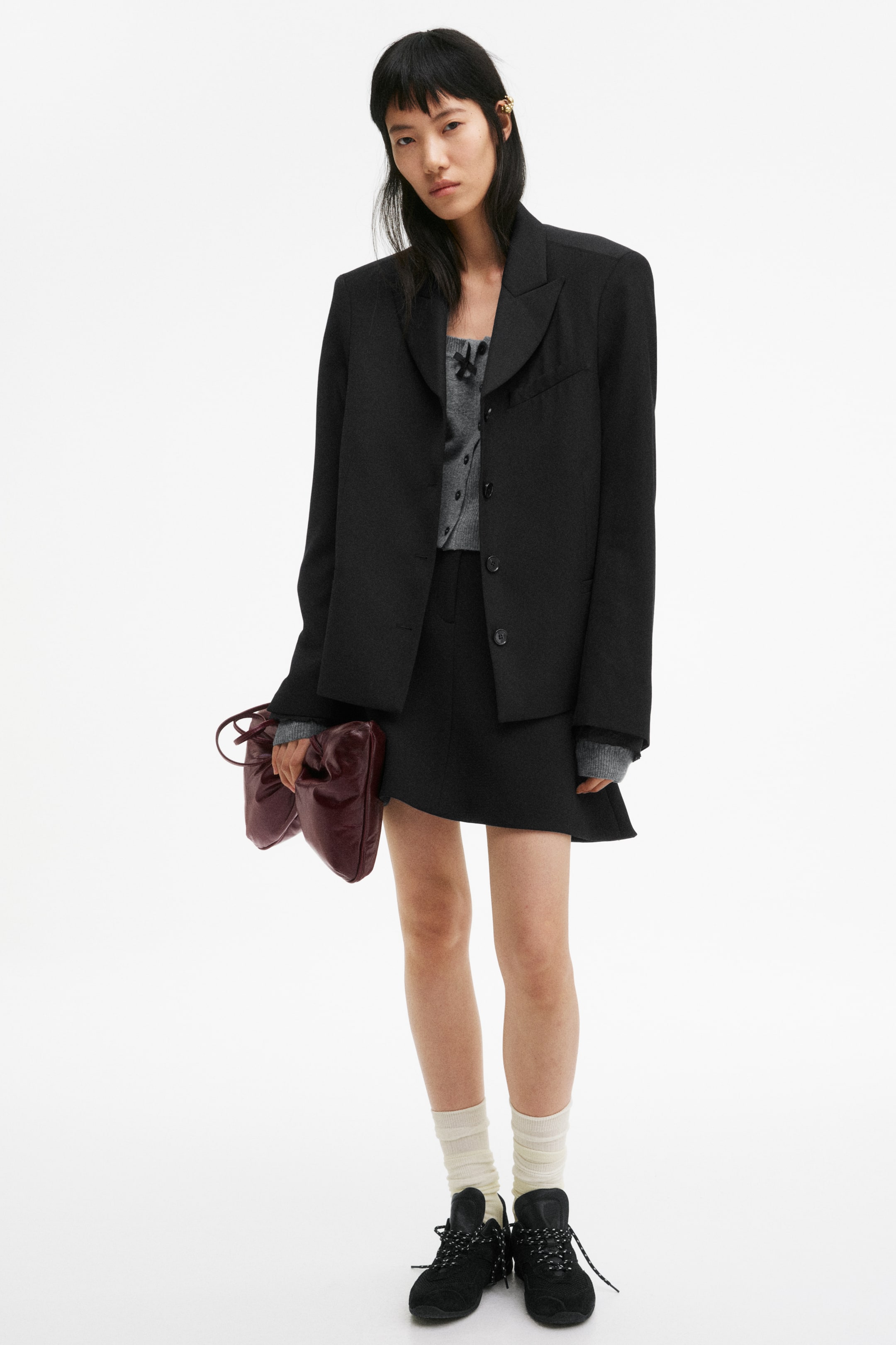 View larger image: The model is wearing a short skirt in a textured weave. It showcases exposed darts at the front, adding to its structured appearance, and features a generous flare at the hem.