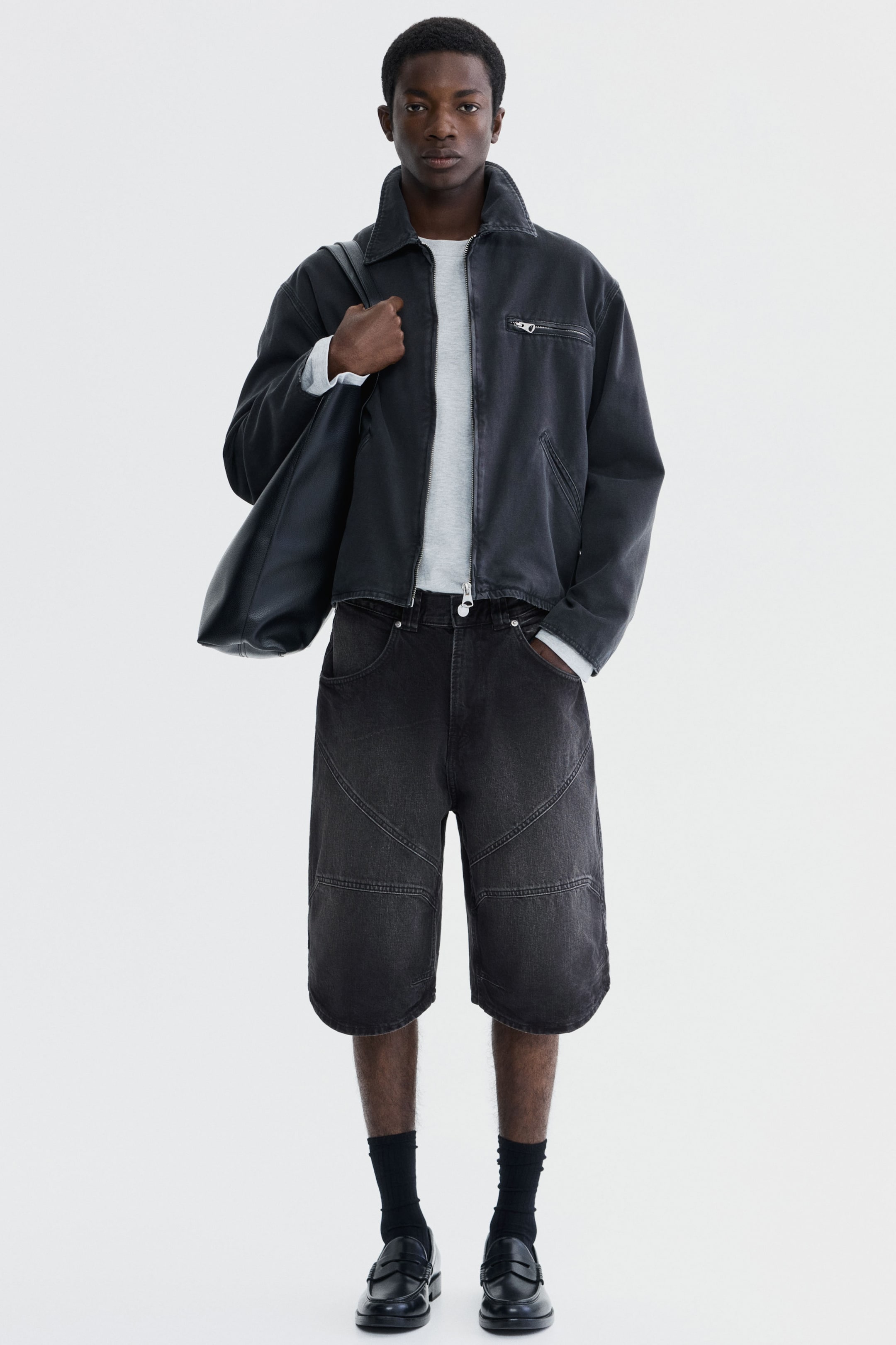 이미지 확대 보기: 모델의 왼쪽 어깨에 걸쳐진 검은색 토트백이 짙은 회색 재킷 위에 놓여 있습니다.