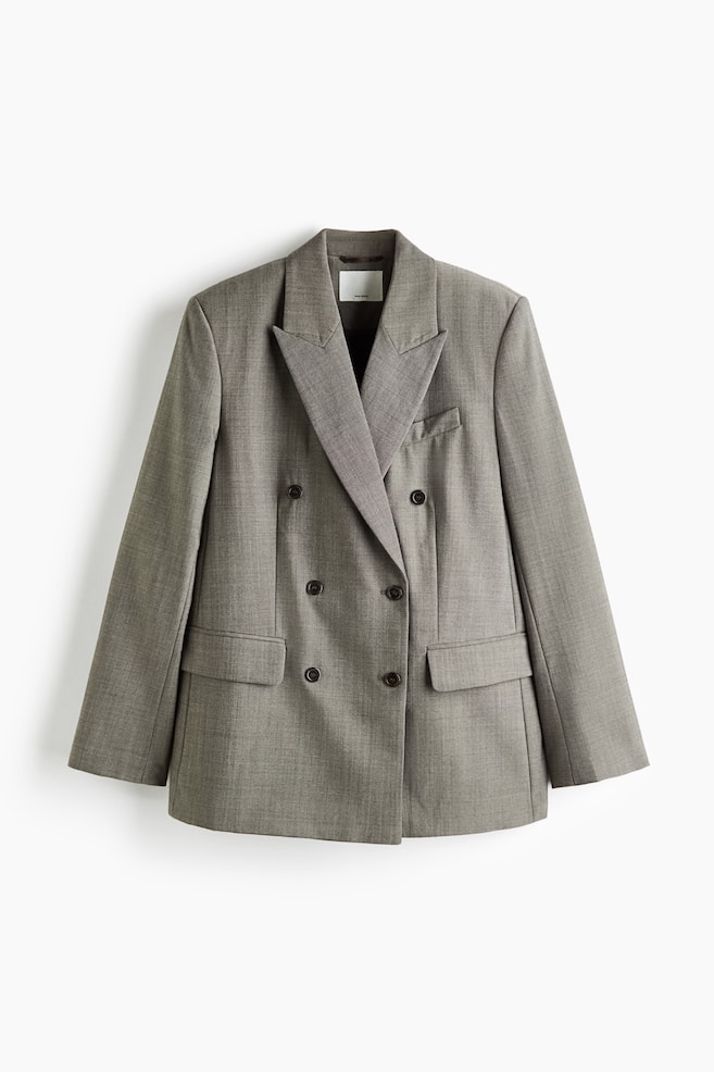Ein grauer Zweireiher-Blazer ist von vorne zu sehen und verfügt über markante fallende Revers sowie einen Sechs-Knopf-Verschluss. Der Blazer zeigt strukturierte Schultern, eine einzelne Brustleistentasche und zwei untere Pattentaschen, alle aus strukturiertem grauem Melange-Stoff gefertigt. - 1