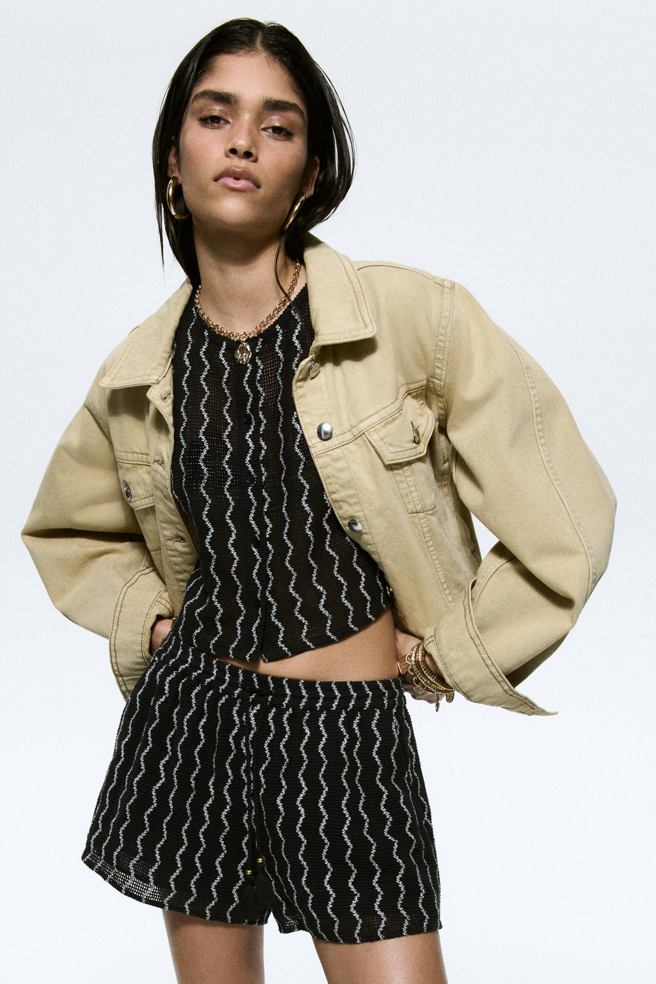 View larger image: A beige cropped denim jacket is featuring a classic collar, chest flap pockets, and visible stitching. 