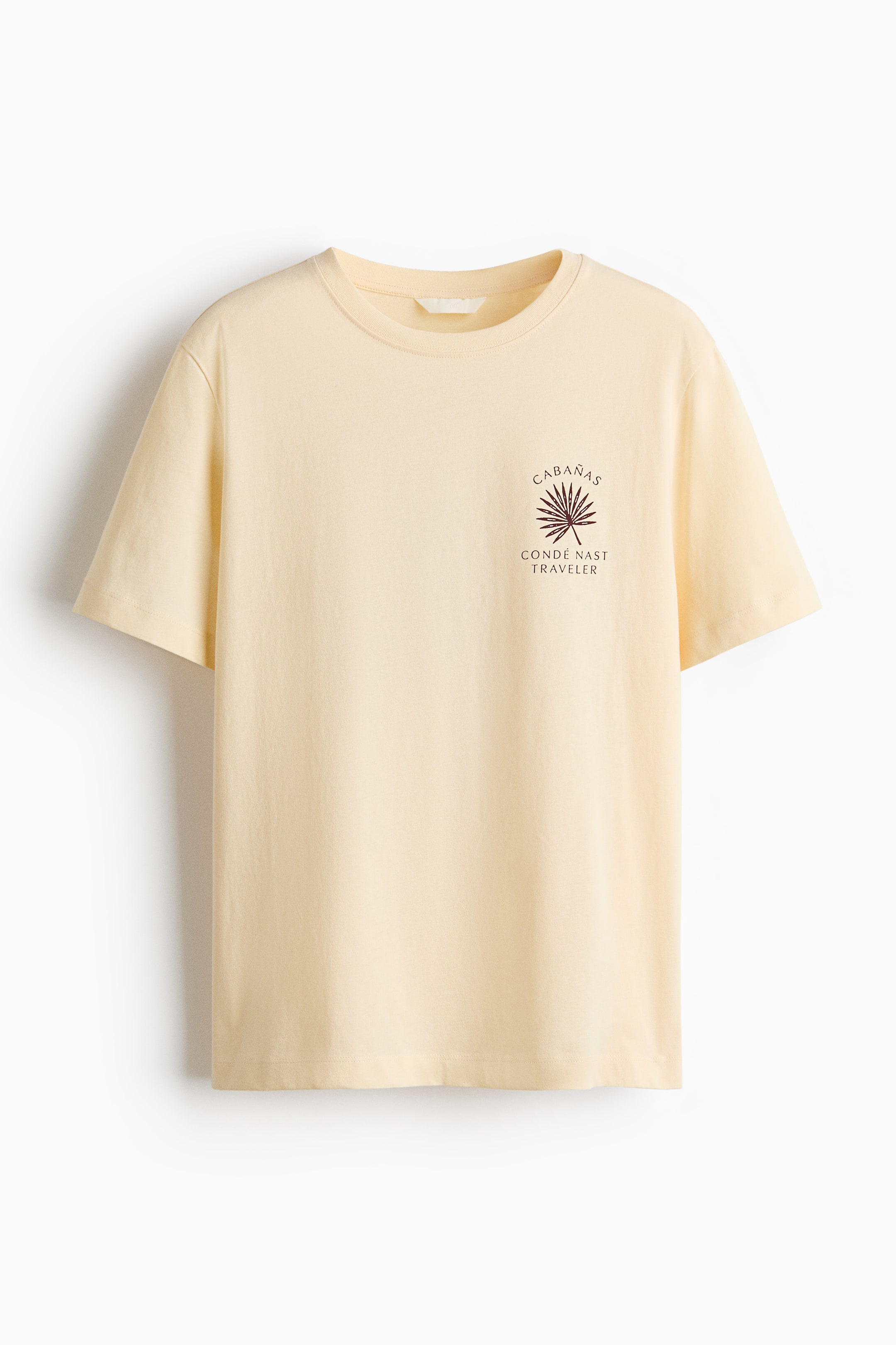View larger image: A pale yellow tee showcases its front, adorned with a dark reddish-brown graphic on the left chest area, displaying "CABANAS" above a palm leaf illustration, with "CONDÉ NAST TRAVELER" beneath it. This round-neck tee is crafted with short sleeves.