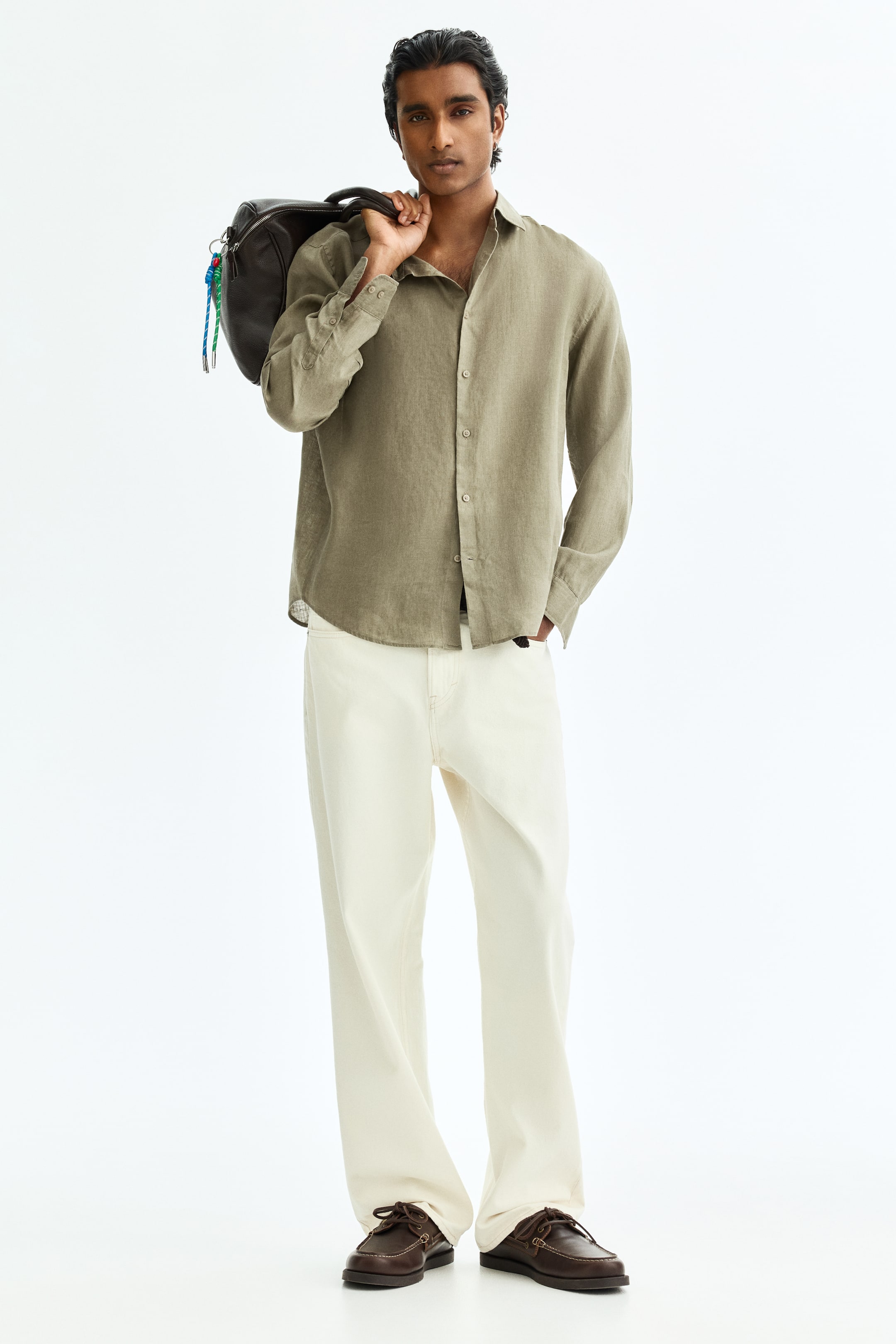 View larger image: A model is showcasing a relaxed-fit olive green long-sleeved shirt featuring a collar and a button-up front, with the top buttons left undone. This is paired with cream wide-leg trousers and dark brown lace-up boat shoes.