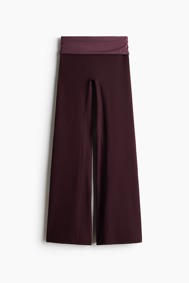 A pair of wide-leg pants is shown from the front, featuring a deep burgundy body and a contrasting, slightly lighter plum-colored fold-over waistband. The pants are hanging straight, showcasing a smooth drape and a relaxed, wide-leg silhouette. - 1