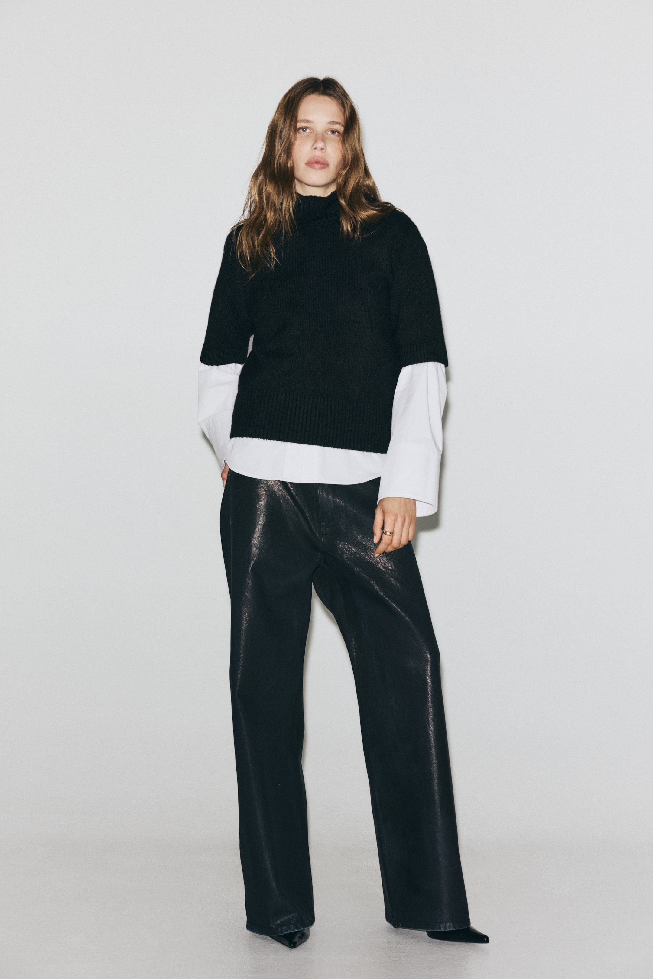 View larger image: A black turtleneck sweater is being presented FRONT, showcasing its relaxed fit and layered design with a white long-sleeved shirt. The sweater is featuring elbow-length sleeves and a ribbed bottom hem, with the white shirt's long sleeves and lower hem visibly extending beneath it.