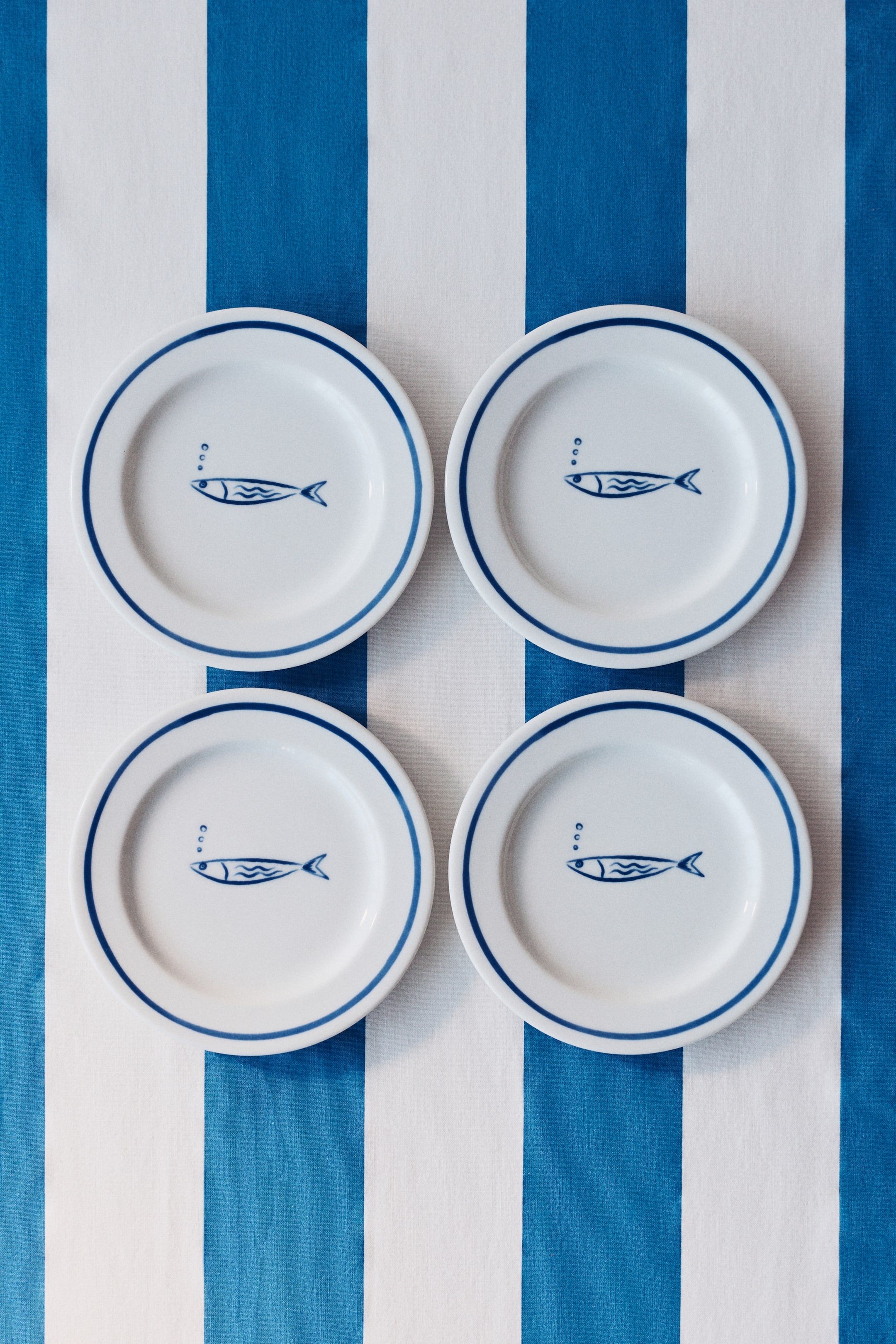 Agrandir l'image: Quatre assiettes rondes blanches sont disposées en grille, chacune arborant un bord bleu foncé et une ligne intérieure bleu foncé. Chaque assiette présente également un motif de poisson stylisé bleu foncé avec trois bulles au centre, le tout vu de dessus.