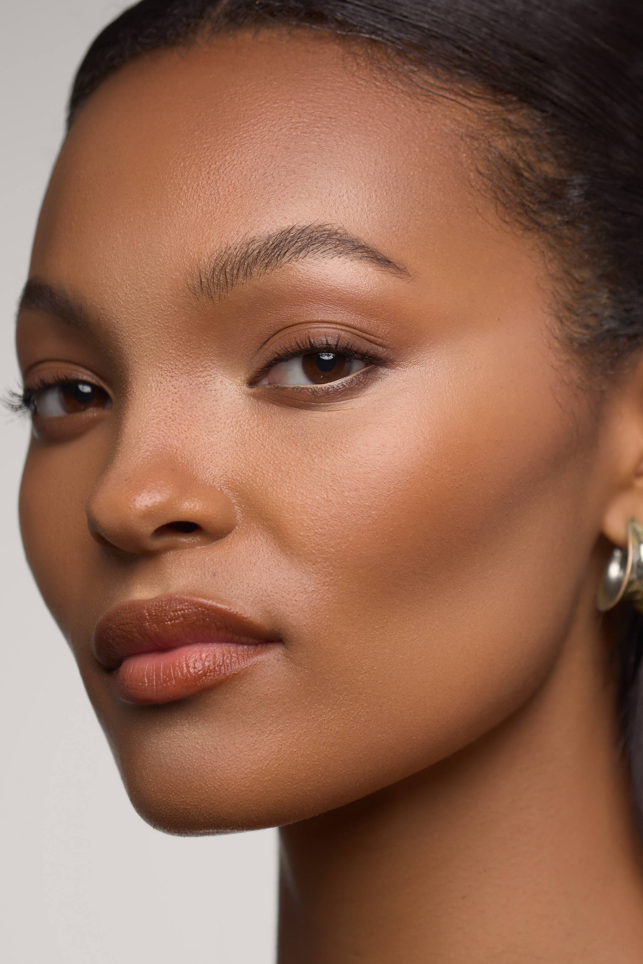 Vis større bilde: Morphe Shapelifter Micro Brightening Stick er vist påført en models ansikt, og gir en jevn, matt highlight til området under øynene, brynsbenet og neseryggen. Den utblendbare, shimmerfrie formelen fremhever den naturlige dimensjonen og strukturen i trekkene hennes.