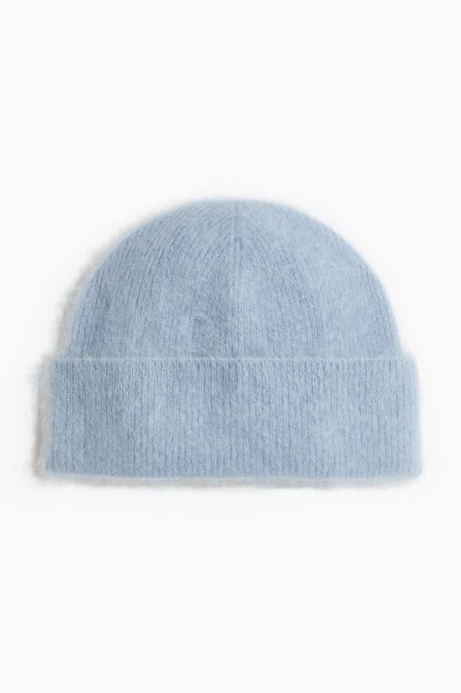 Un bonnet en maille bleu clair est prÃ©sentÃ© de face, avec une texture duveteuse et brossÃ©e ainsi quâun large revers retroussÃ©. Le bonnet est conÃ§u avec une calotte arrondie, mettant en valeur sa matiÃ¨re en maille douce et moelleuse. - 1