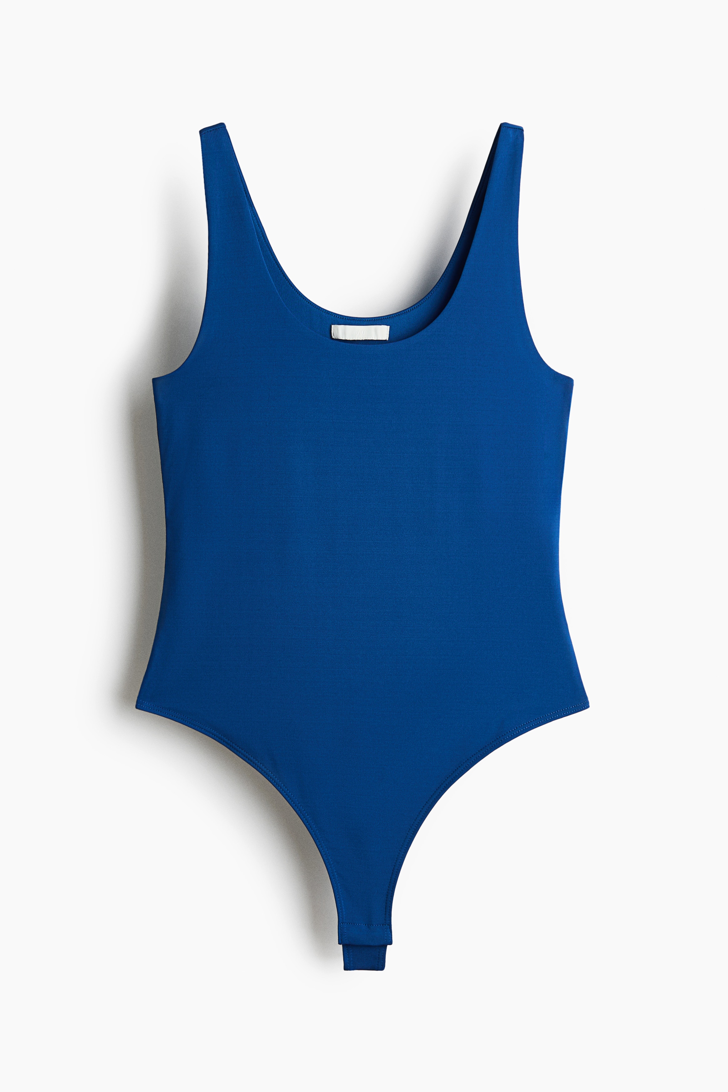 La modelo lleva un body azul de jersey elÃ¡stico con cuello redondo y tirantes anchos. El body estÃ¡ metido dentro de un pantalÃ³n blanco de tiro alto y se lleva debajo de una camisa abotonada abierta de rayas azules y blancas.
