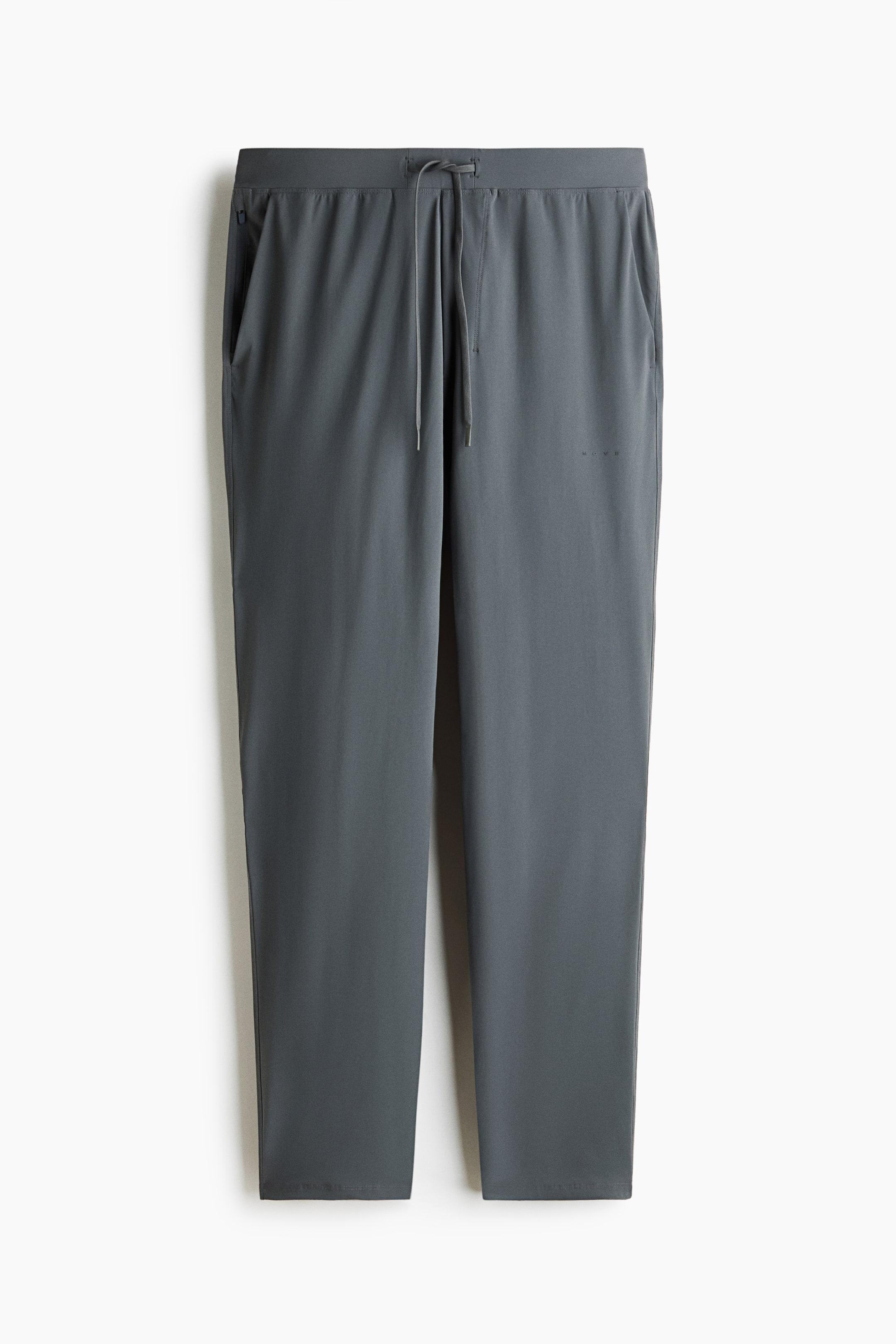 View larger image: Dark grey pants are showcased from the front, featuring an elasticated waistband with a visible drawstring. Two side pockets are visible, with the left one displaying a zipper closure, while a subtle logo appears on the upper right thigh, and the legs end in a plain hem.