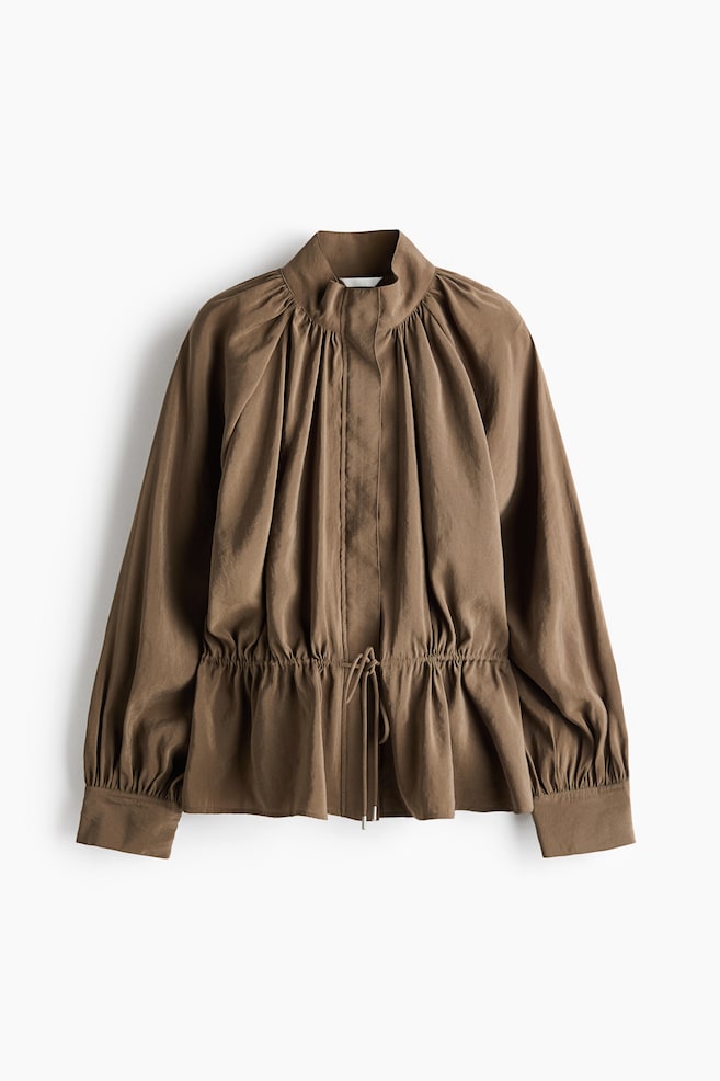 A brown modal-blend jacket is shown facing front, featuring a high stand collar, a concealed front placket, and gathered raglan balloon sleeves with wide cuffs. The jacket is cinched at the waist by an adjustable drawstring with tied cords, creating a gathered effect that flares out into a peplum hem. - 1