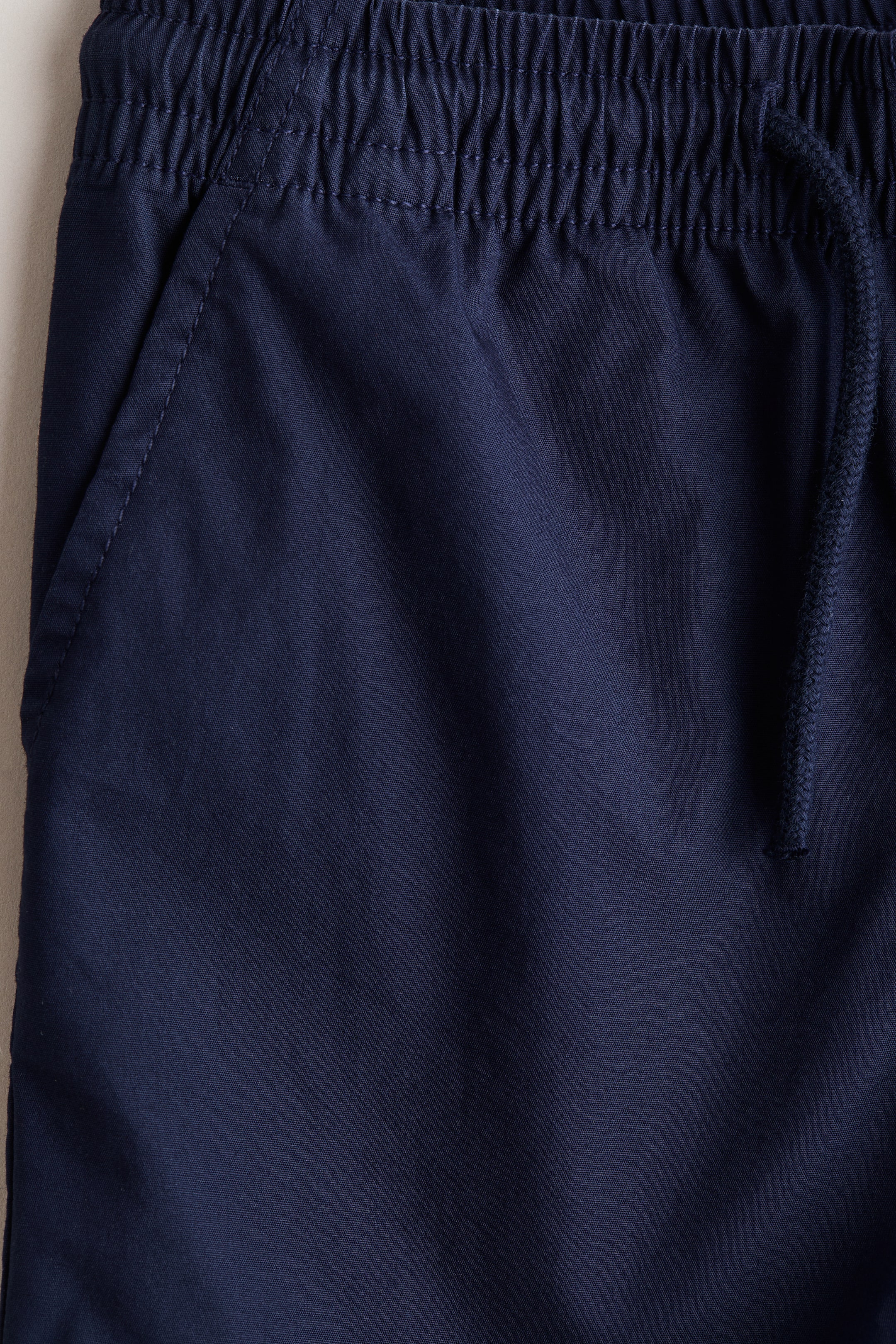 Visualizza l'immagine ingrandita: Shorts blu navy con vita elasticizzata in tessuto arricciato e cordoncino intrecciato a destra. Una tasca laterale angolata è visibile a sinistra, delineata con cuciture.