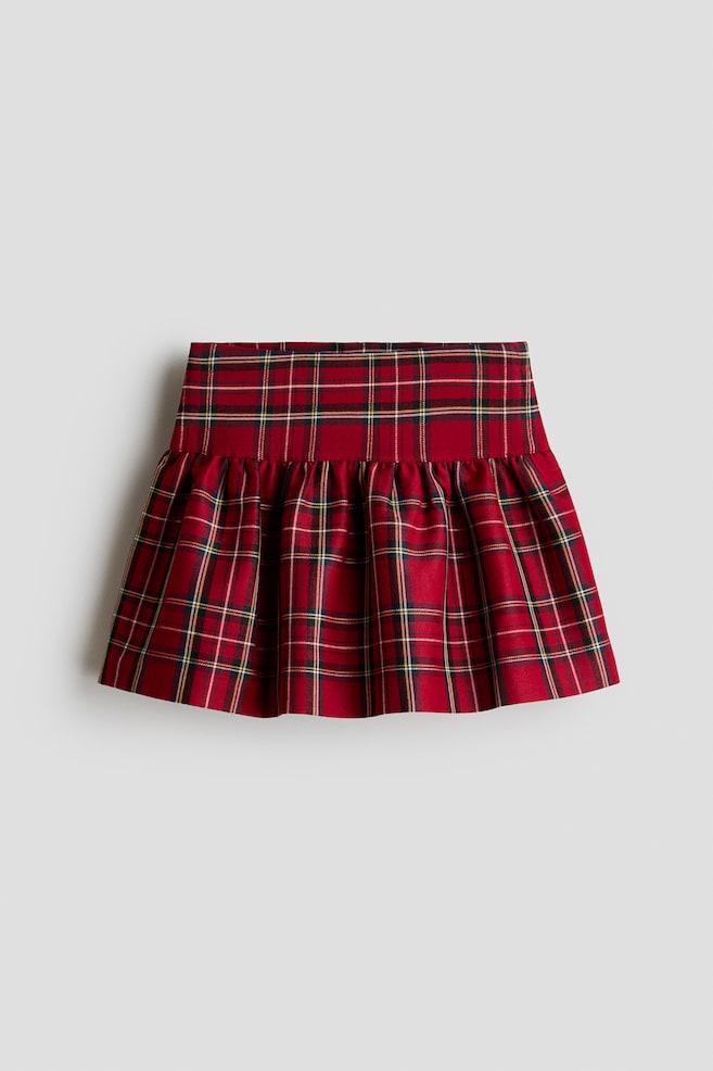 Czerwona spódnica w tartan jest pokazana od przodu, eksponujÄ
c szeroki, pÅaski pas oraz marszczony, rozkloszowany dóÅ. Ubranie prezentuje klasyczny wzór w kratÄ z czerwonymi, czarnymi, biaÅymi i żóÅtymi liniami. - 1