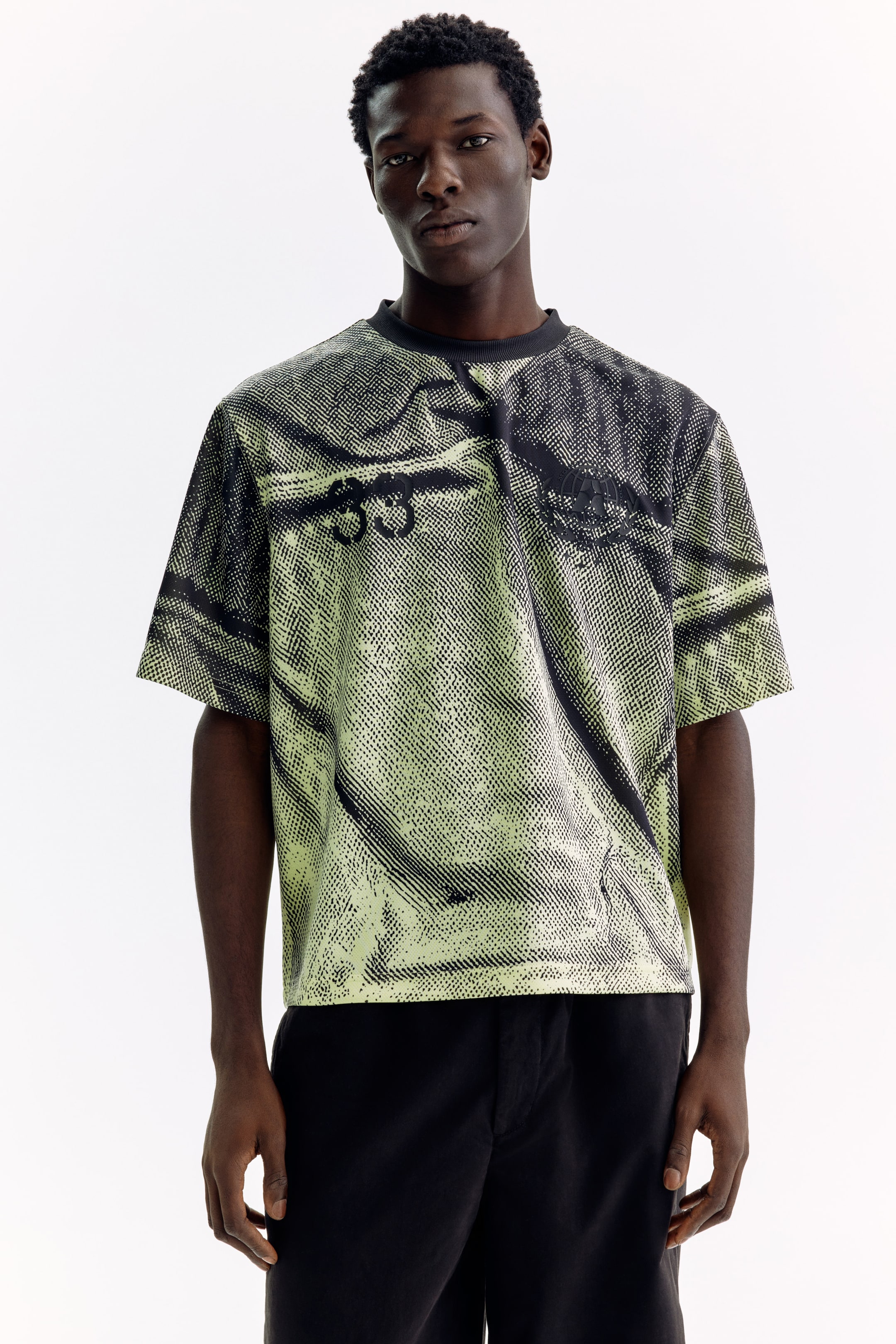 View larger image: A front-facing, short-sleeved t-shirt featuring a black crew neck and a lime green base with a black halftone graphic print. The print displays abstract shapes and the numbers "33" across the chest.