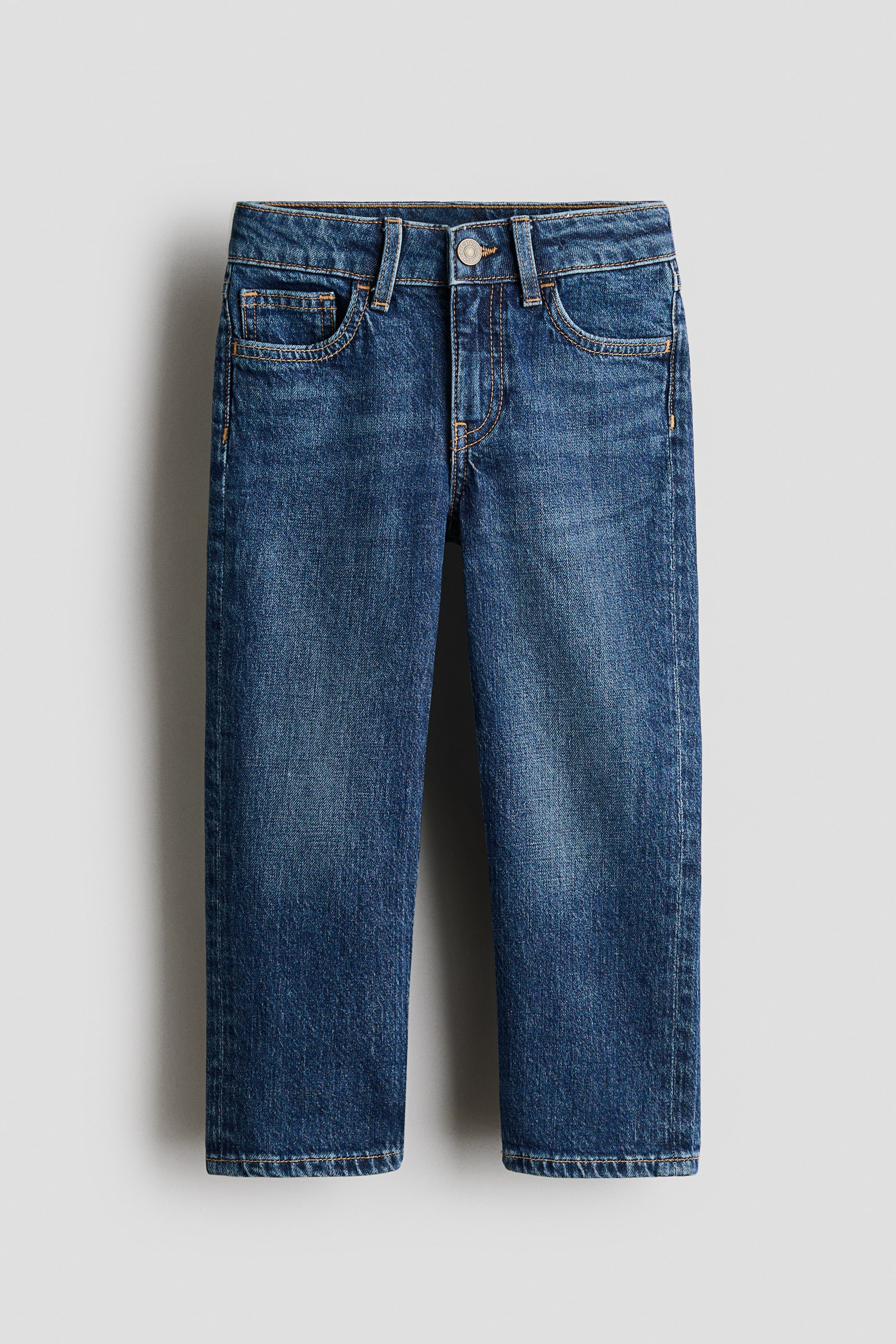 Xem ảnh lớn hơn: Quần jeans denim xanh 5 túi được trưng bày từ phía trước, có kiểu dáng thoải mái qua hông, đùi và chân. Chúng có khóa kéo với nút cài, các vòng đai, túi trước và túi tiền xu có đường chỉ nổi màu cam, và phần phai nhẹ ở đùi.