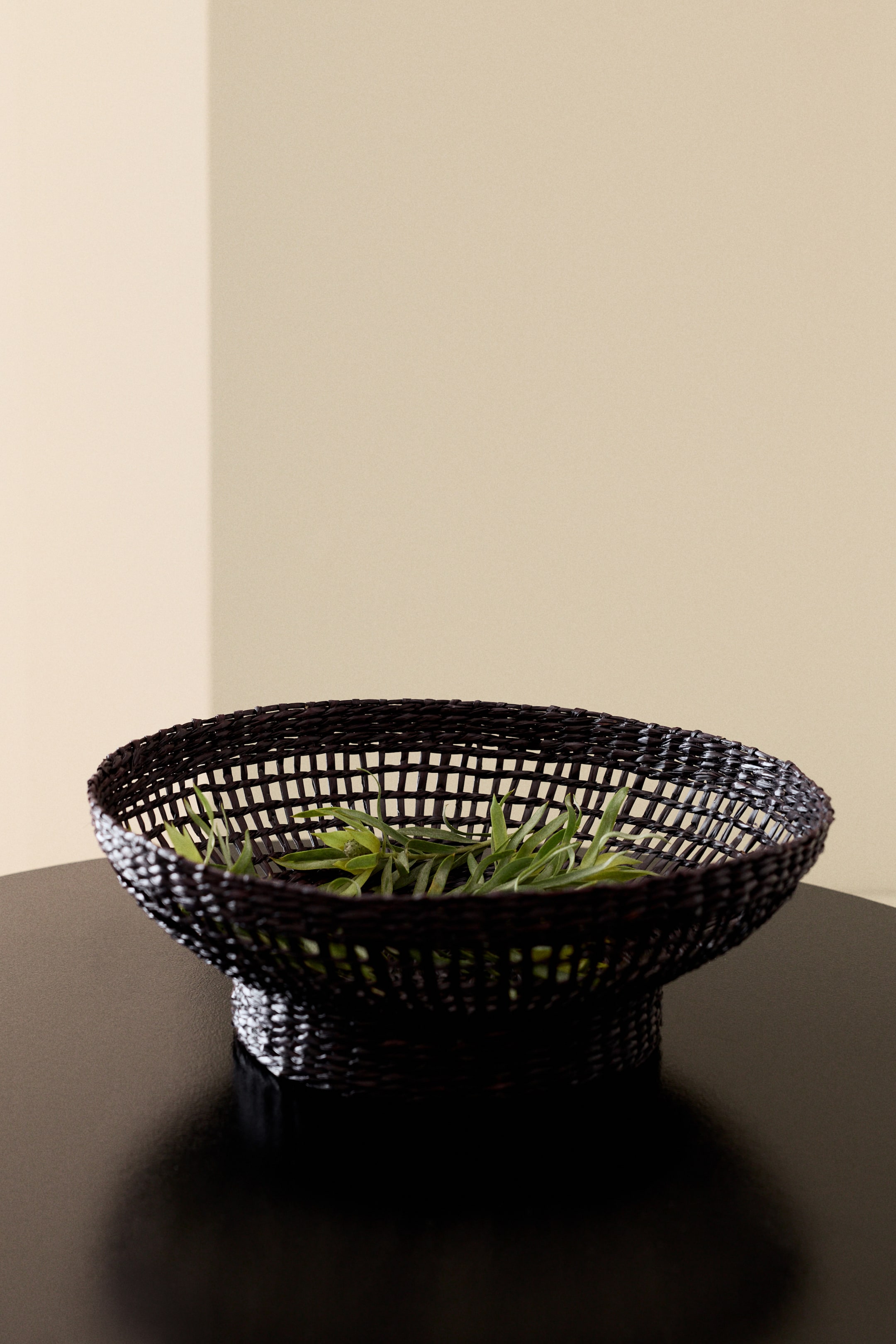 View larger image: A dark, braided seagrass bowl showcasing an open-weave design, elegantly flaring out from a narrower base, with green leaves nestled inside.