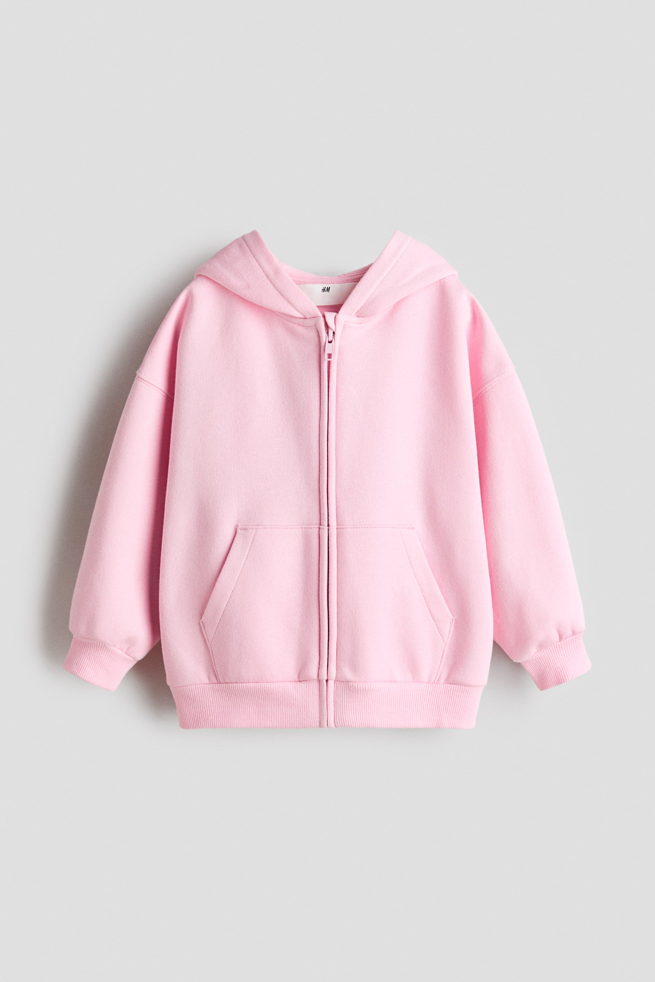 Ver imagen más grande: Una sudadera con capucha rosa de corte oversize con cremallera frontal muestra su parte delantera; presenta capucha, una cremallera que recorre el centro, hombros caídos, mangas largas y dos bolsillos tipo canguro delanteros. Puños y bajo de canalé completan la prenda.