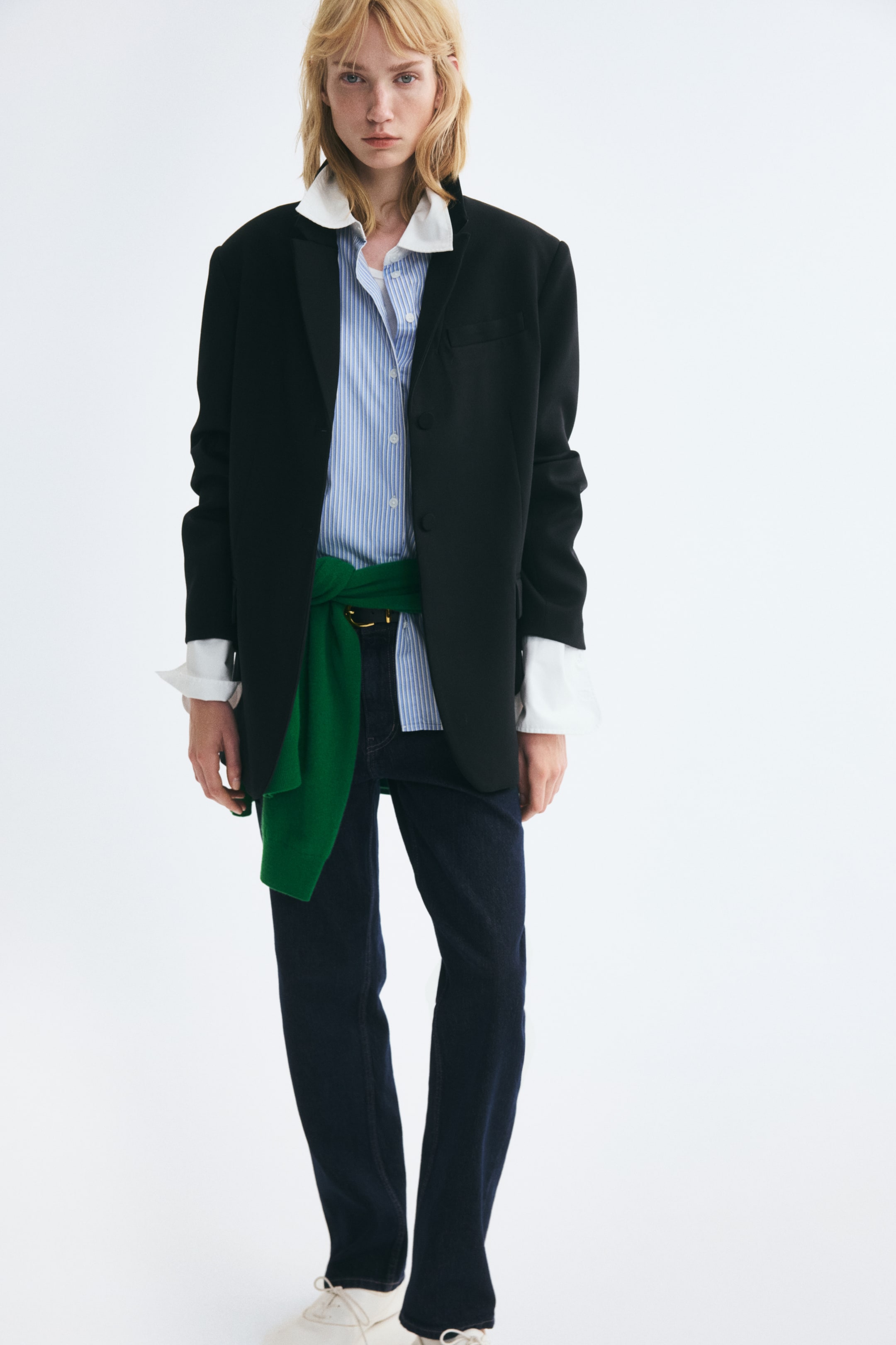 Vis større bilde: Mørkeblå denimjeans med regular fit og avsmalnede ben bæres av modellen. Jeansene med høyt liv er stylet med et svart belte, en blå- og hvitstripete skjorte, en oversized svart blazer og en grønn genser knyttet rundt livet.