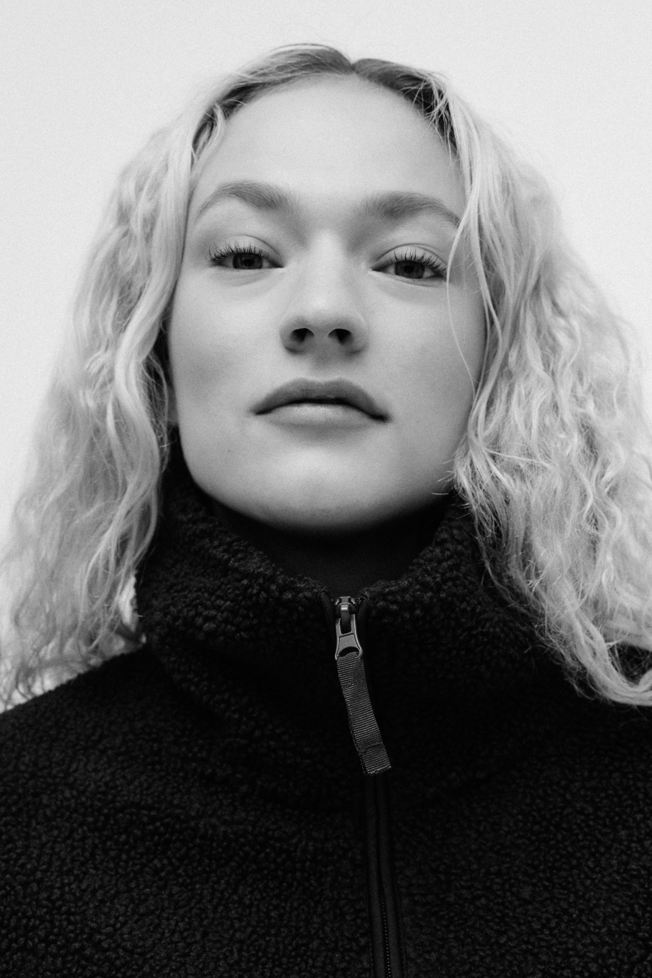 Se større billede: En jakke i blødt teddy bæres af modellen. Den høje krave er lynet op, dækker modellens hals, og en lynlås trækker er synlig.