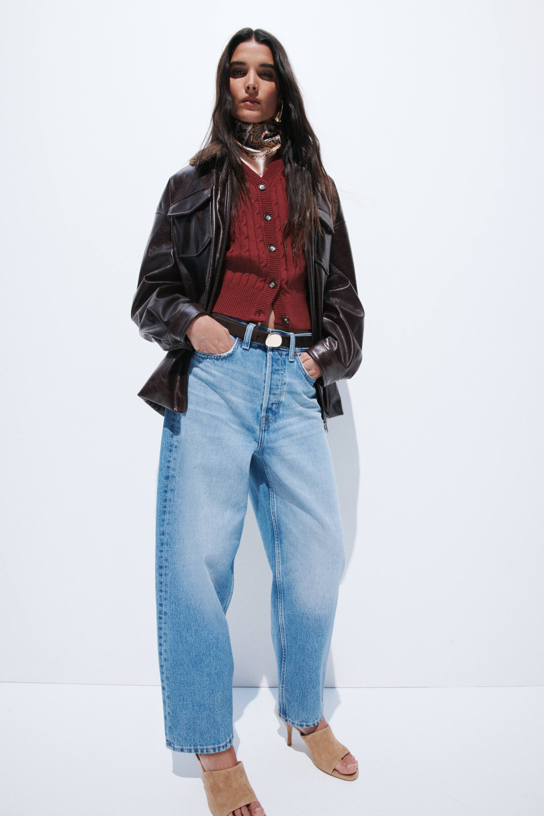View larger image: A dark brown leather jacket is being worn, featuring a prominent collar with a visible faux fur lining and chest flap pockets. It presents a relaxed fit and is styled open, revealing its front zip closure.