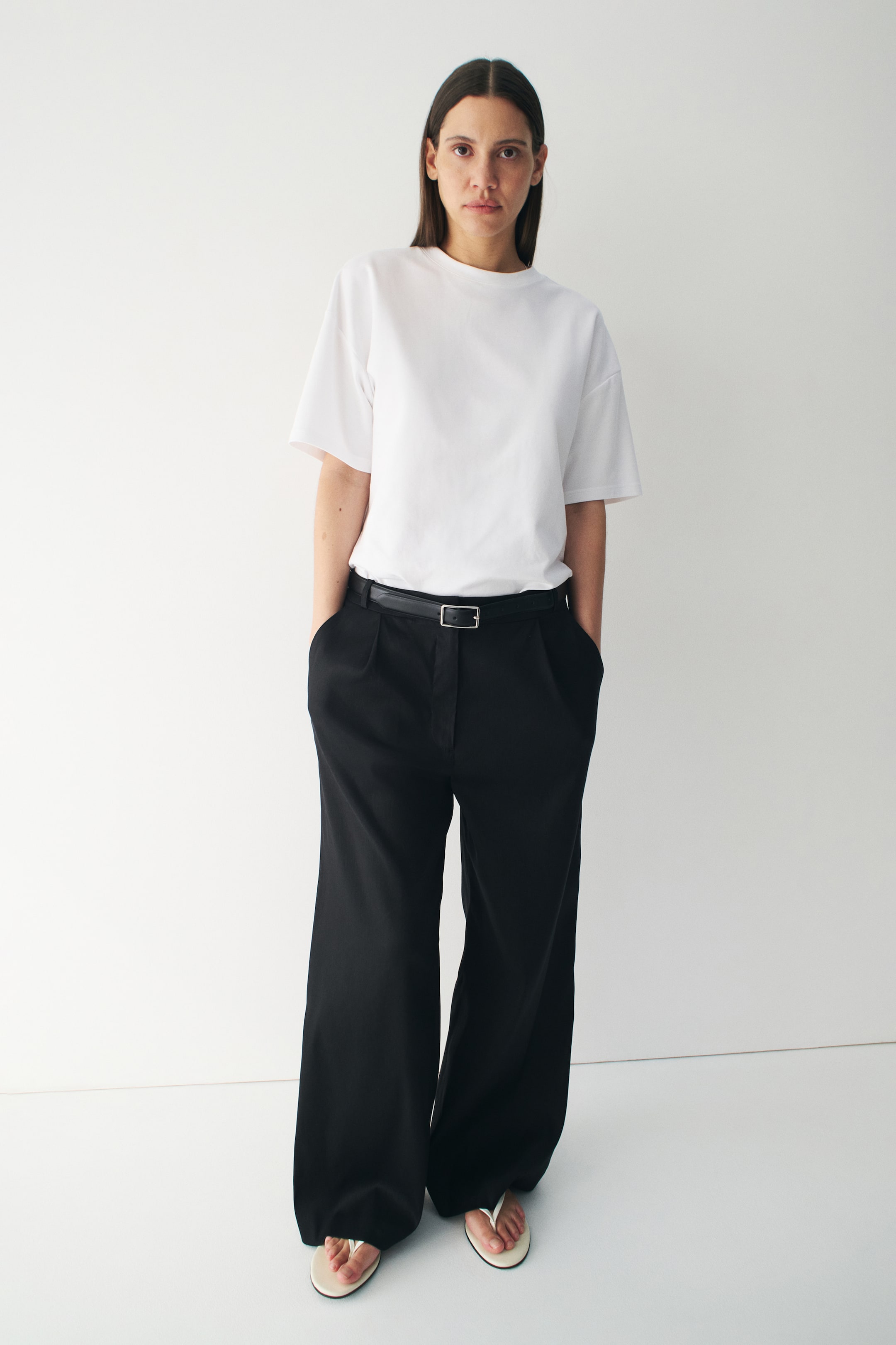 View larger image: The white t-shirt is facing forward, showcasing a relaxed fit and a crew neck. It boasts short, loose sleeves and is tucked into black trousers, highlighting a smooth fabric texture.