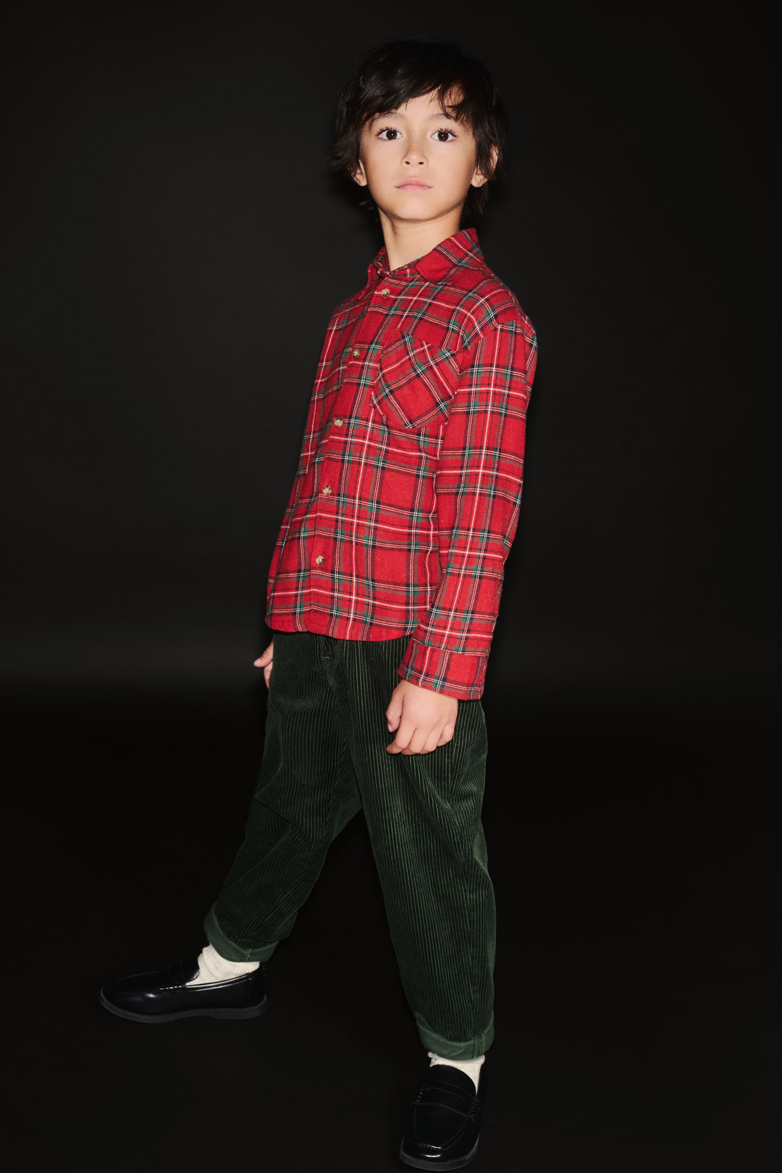 A loose-fit red plaid flannel shirt is being presented from the front, featuring a collar, buttons running down its front, dropped shoulders, long sleeves ending in buttoned cuffs, and an open chest pocket situated on the left side, with its hem gently curving. - 1