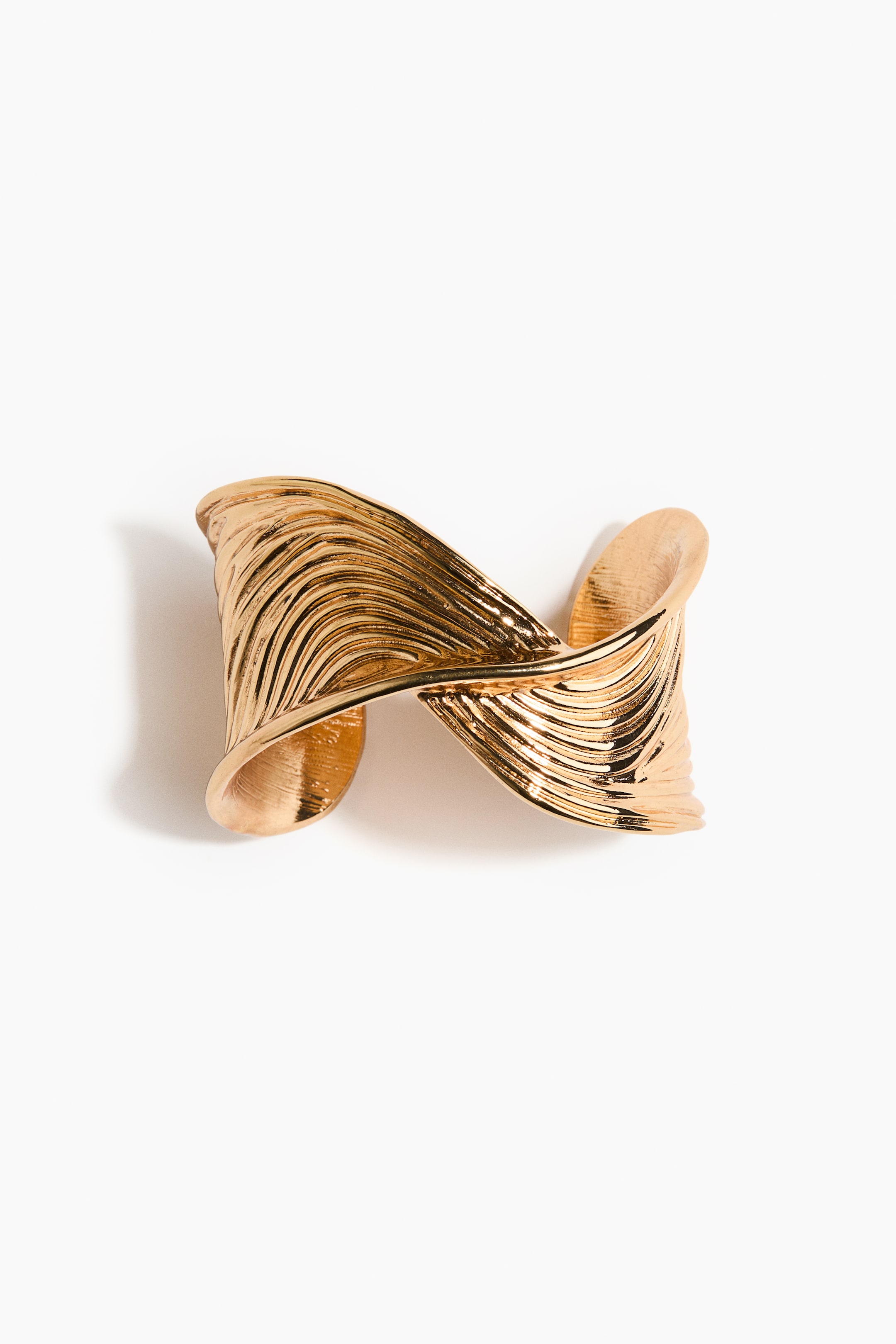View larger image: A gold-colored cuff bracelet is displaying a wide, sculptural form, featuring a twisted center and a wavy, grooved texture across its surface, presented from the front.