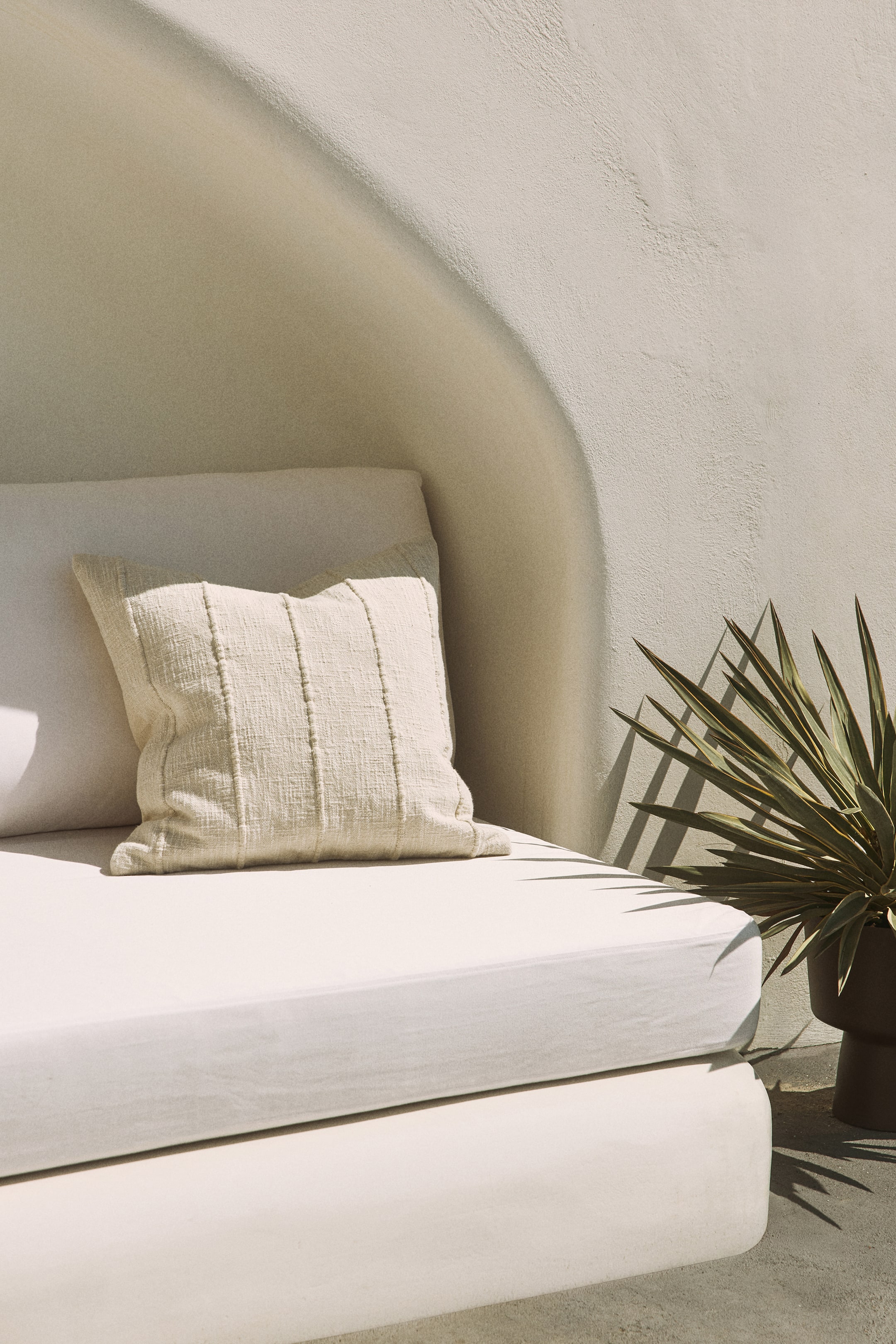 View larger image: A square cushion crafted from cream woven fabric rests against a lighter back cushion. It showcases five distinct vertical stitched lines running across its front surface.