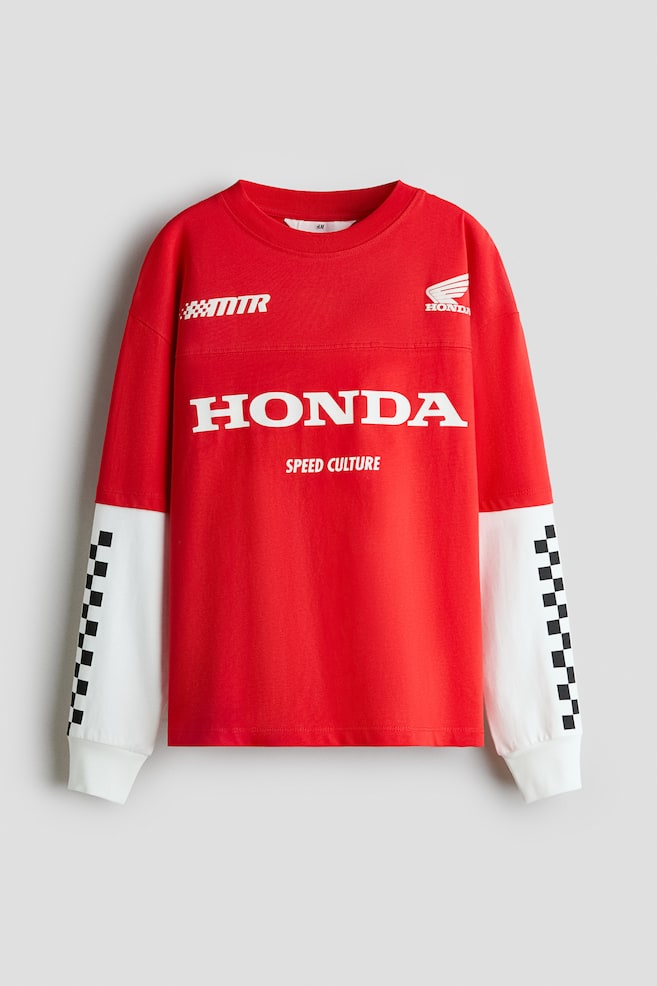 Czerwony T-shirt o luźnym kroju jest pokazany z przodu, z warstwowÄ
konstrukcjÄ
, w której spod czerwonych krótkich rÄkawów wystajÄ
biaÅe dÅugie rÄkawy. Model ma opuszczonÄ
liniÄ ramion, okrÄ
gÅy prÄ
żkowany dekolt, widoczne poziome przeszycie na wysokoÅci klatki piersiowej oraz biaÅe nadruki graficzne, w tym logo âHONDAâ z przodu. BiaÅe dolne rÄkawy zostaÅy wykoÅczone czarno-biaÅym wzorem w kratÄ po bokach oraz prÄ
żkowanymi mankietami. - 1
