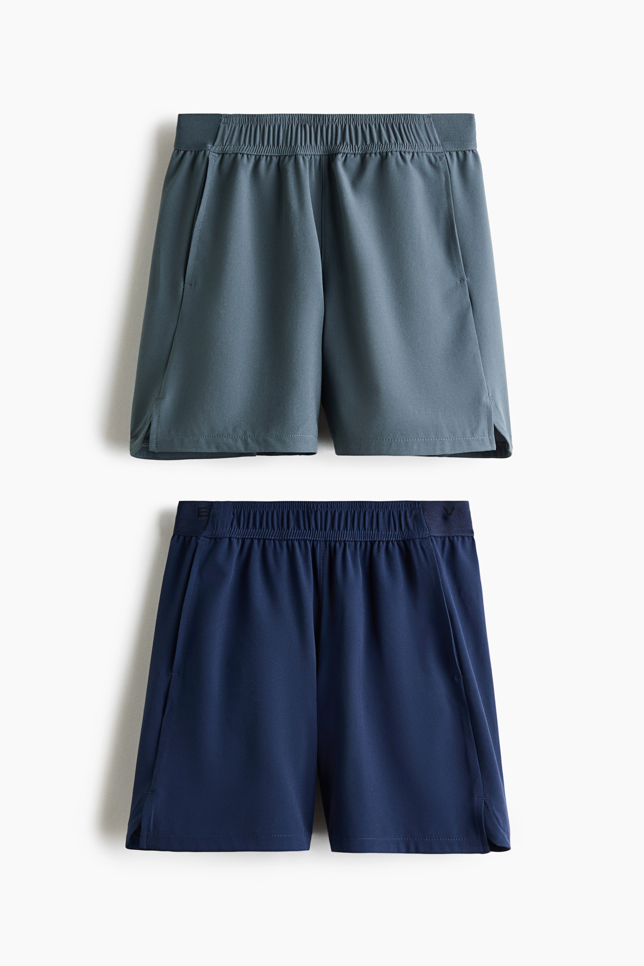Visa större bild: Tvåpack fyrvägsstretchshorts med DryMove presenteras som ett par i mörk teal och ett par i marinblå, staplade vertikalt och vända framåt. Båda shortsen har elastiska midjeband, sidofickor och små sidoslitsar vid fållen, tillverkade av ett slätt tyg.