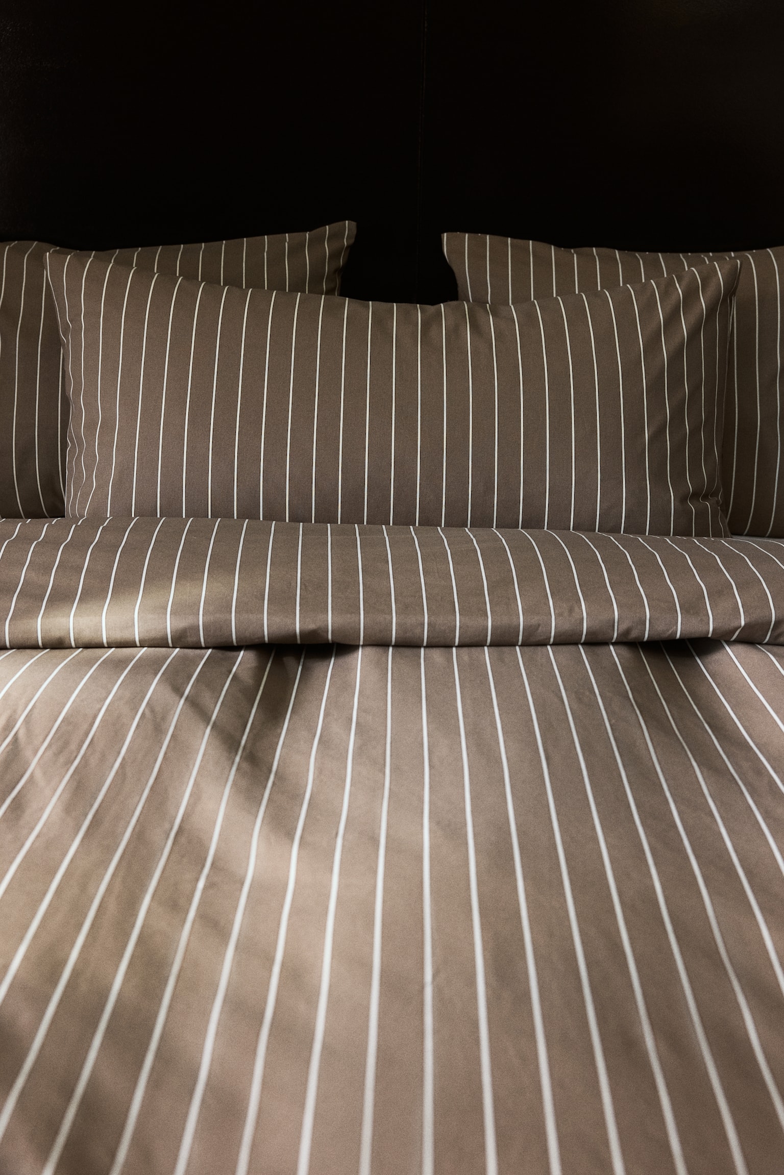 Deux taies dâoreiller en coton tissÃ© brun, ornÃ©es de fines rayures blanches verticales, sont prÃ©sentÃ©es de face, placÃ©es derriÃ¨re une housse de couette pliÃ©e dans le mÃªme motif rayÃ© coordonnÃ©. - 1