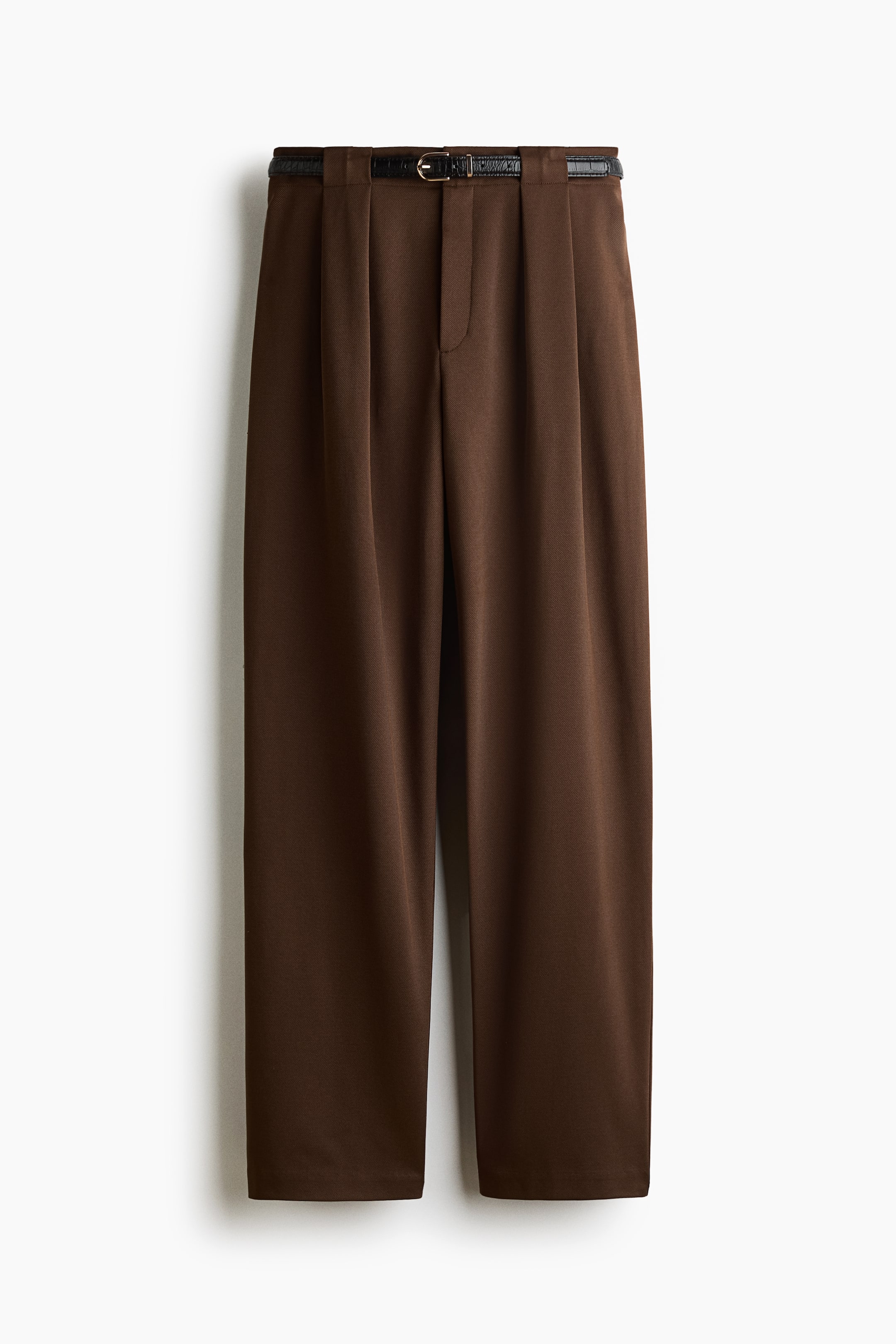 Grösseres Bild ansehen: Eine braune, maßgeschneiderte Hose ist von vorne zu sehen und verfügt über einen hoch geschnittenen Bund mit Falten vorne sowie schmal zulaufenden Beinen. Die Hose ist mit einem abnehmbaren schwarzen Gürtel mit strukturierter Oberfläche und einer Metallschnalle in Goldoptik kombiniert.