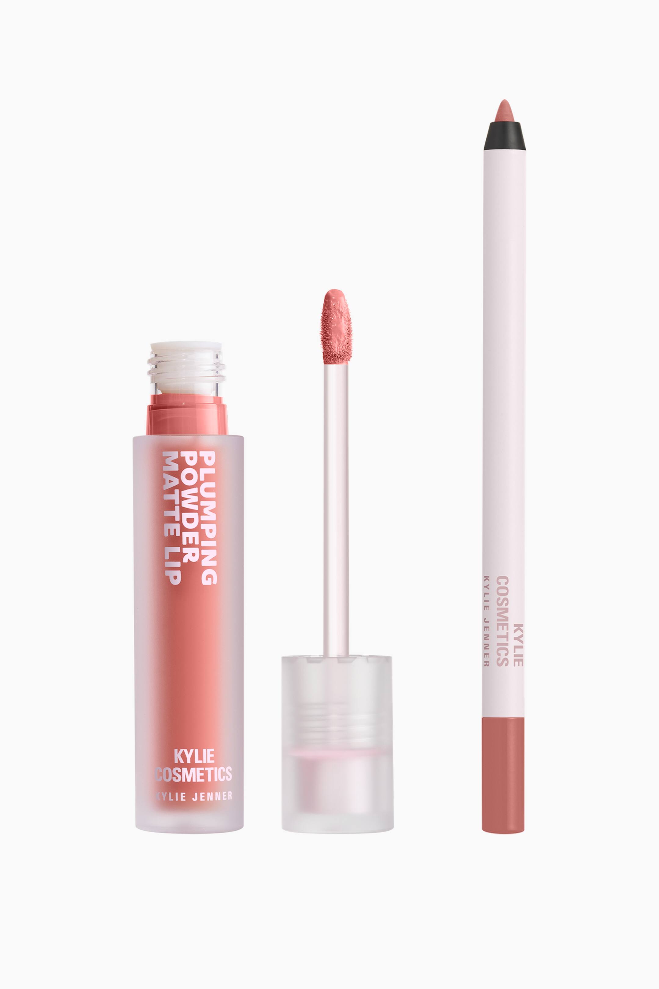 Visa större bild: Kylie Cosmetics Plumping Matte Lip Kit visar ett flytande läppstift, en applikatorstav och en läppenna i en dammig persikoton. Det frostade röret med flytande läppstift och dess upprätta applikatorstav står bredvid en smal, vit läppenna med en matchande persikofärgad spets.