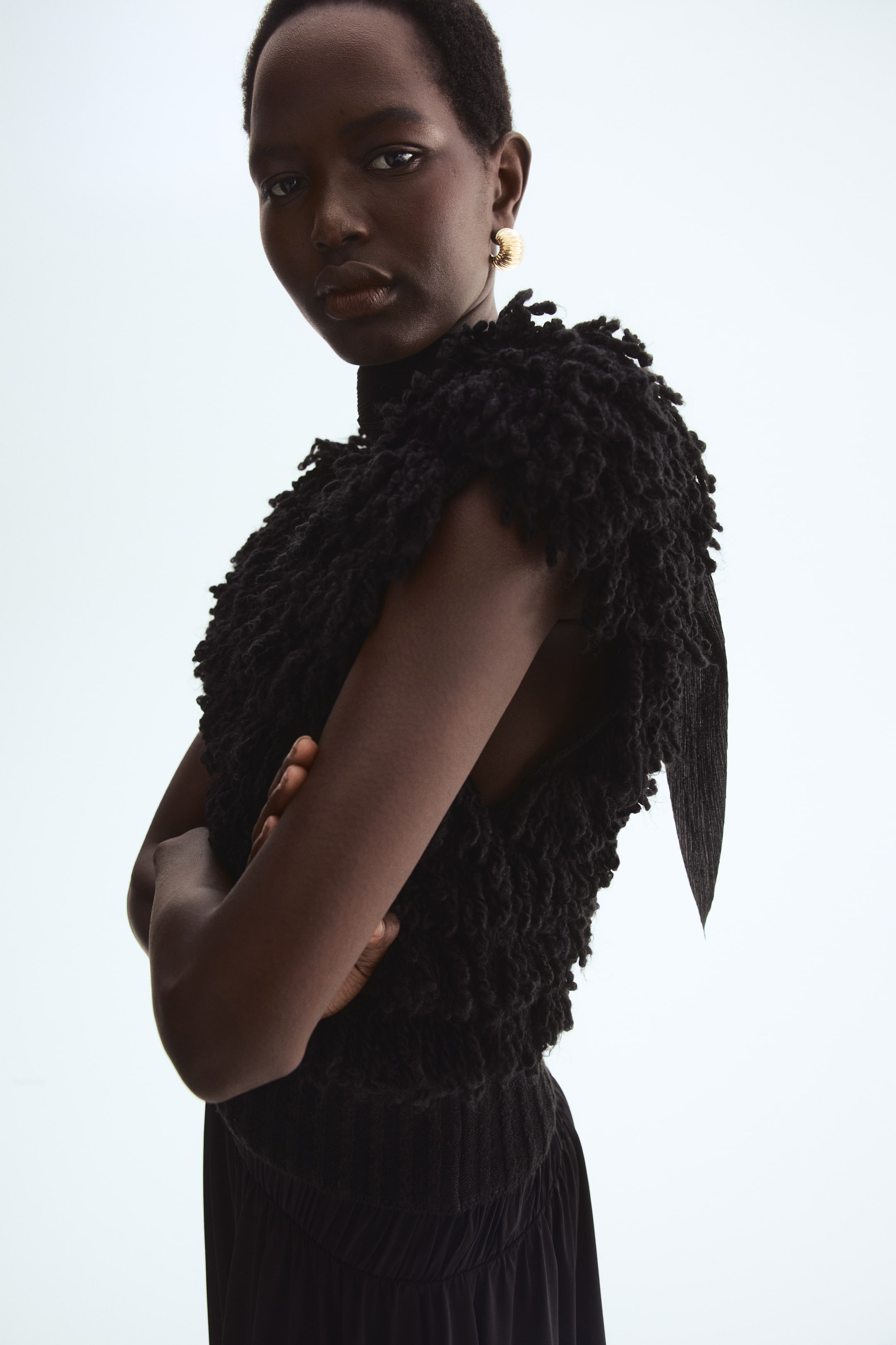 Visa större bild: Ett svart ärmlöst linne med en rufsig, öglad textur över sin huvuddel och en hög halsringning. En platt, spetsig tygdetalj sträcker sig från sidan, och nederkanten är rynkad.