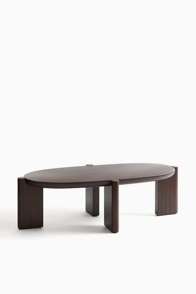 A dark brown oval wooden coffee table featuring a thick, smooth top. It rests on four solid, thick panel legs with rounded edges, with two positioned at each end and two centrally. - 1