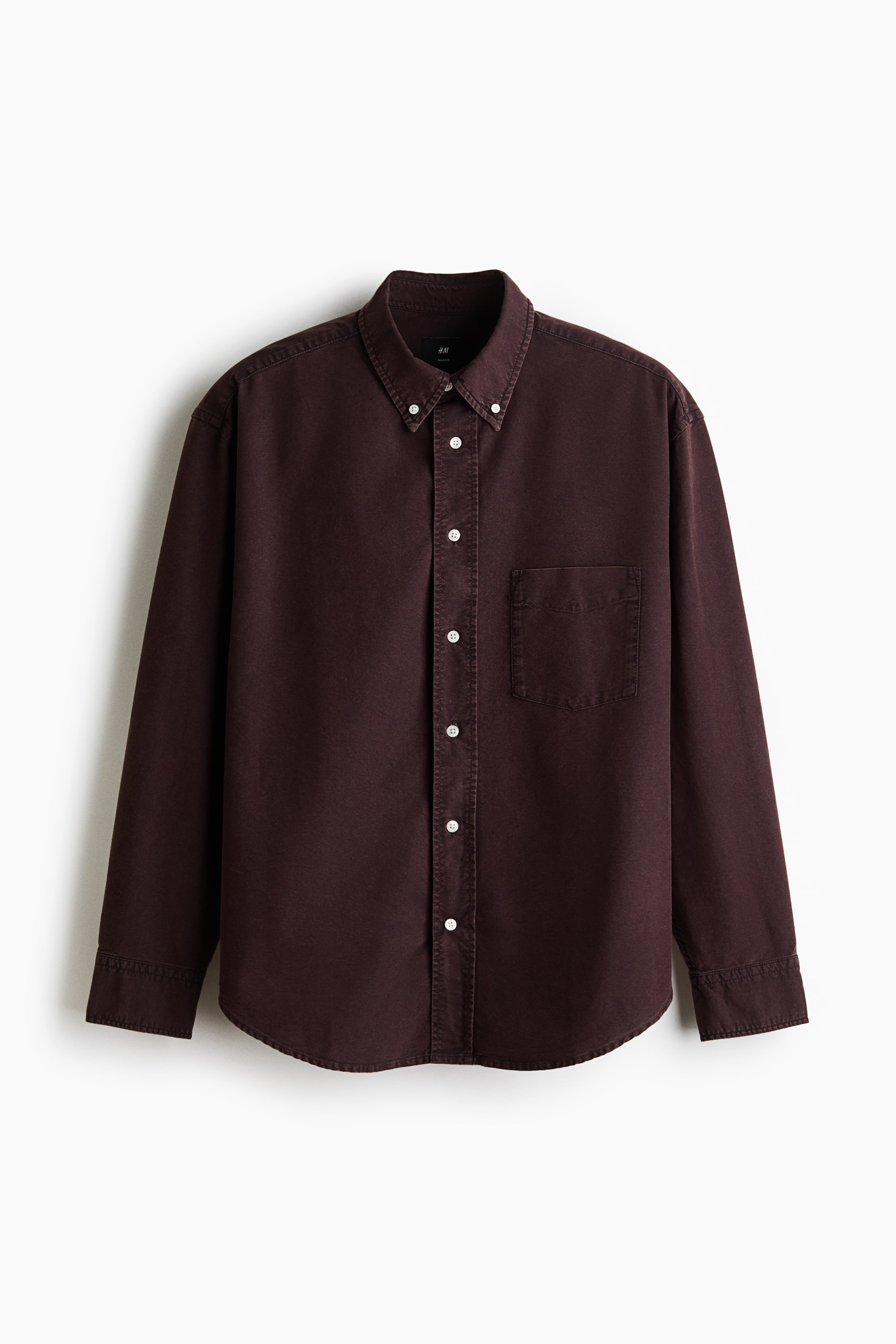View larger image: A dark brown Oxford cotton shirt is showcasing its front view, highlighted by a button-down collar and a classic button placket with white buttons. The long sleeves come with buttoned cuffs and sleeve plackets, each featuring a visible button. An open chest pocket on the left side and a gently rounded hem contribute to its relaxed fit.